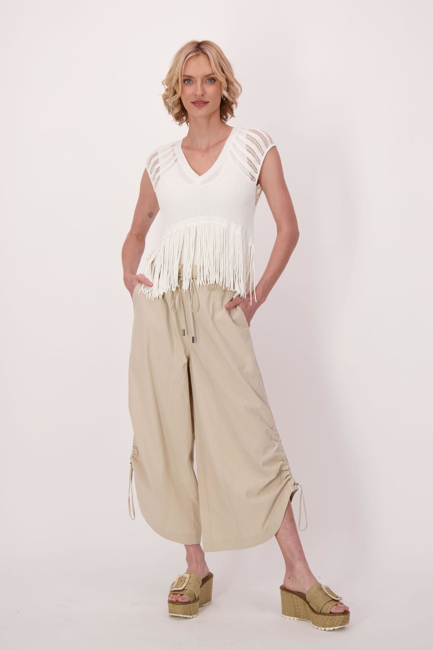 Woman wearing a white fringe top and beige wide-leg pants on a white background