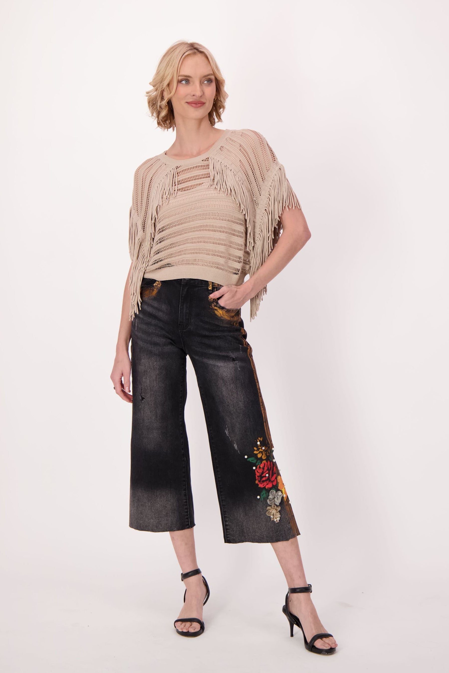 Woman wearing a beige top and black pants with floral embroidery on a white background
