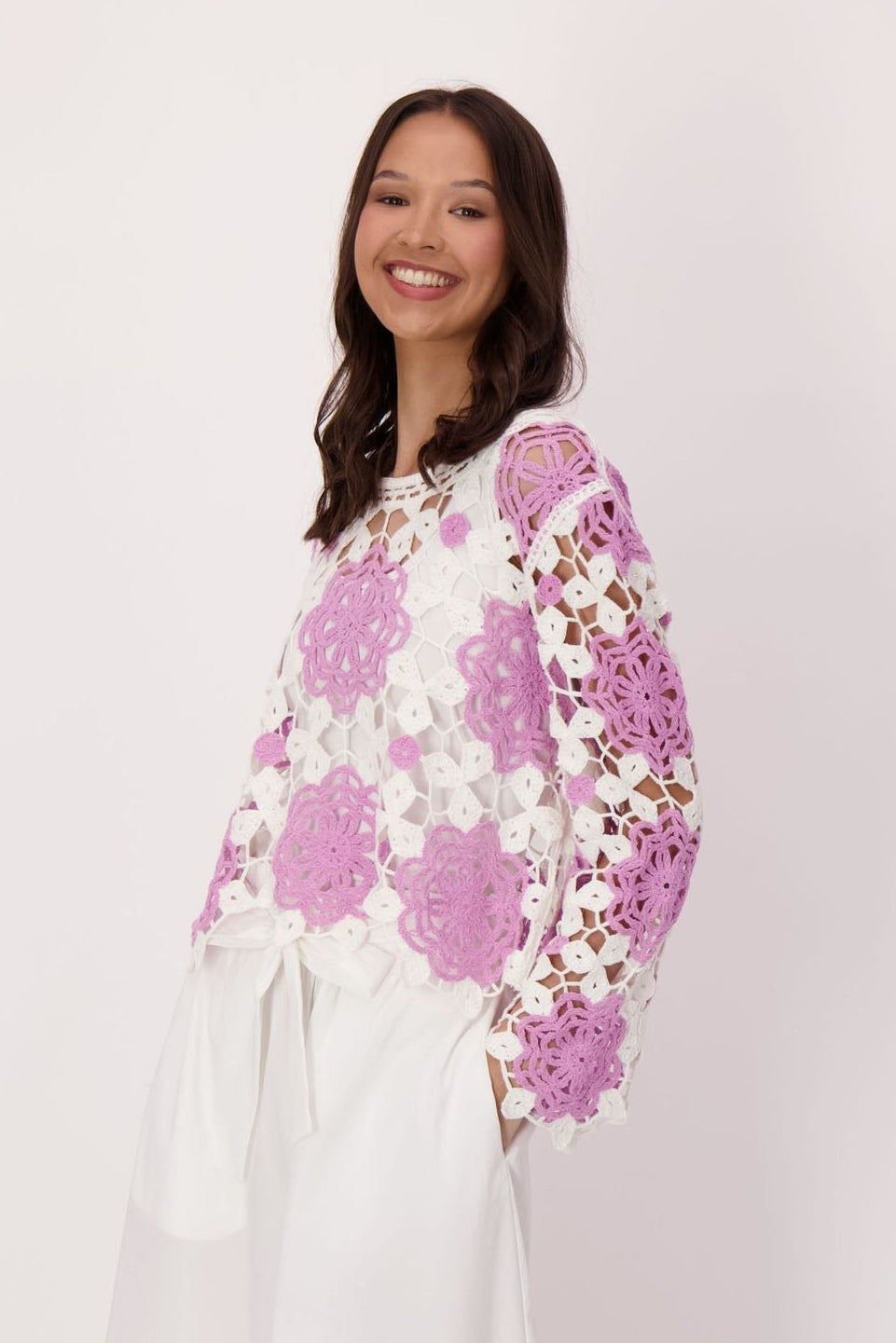 Woman wearing a floral blouse and white pants against a light pink background