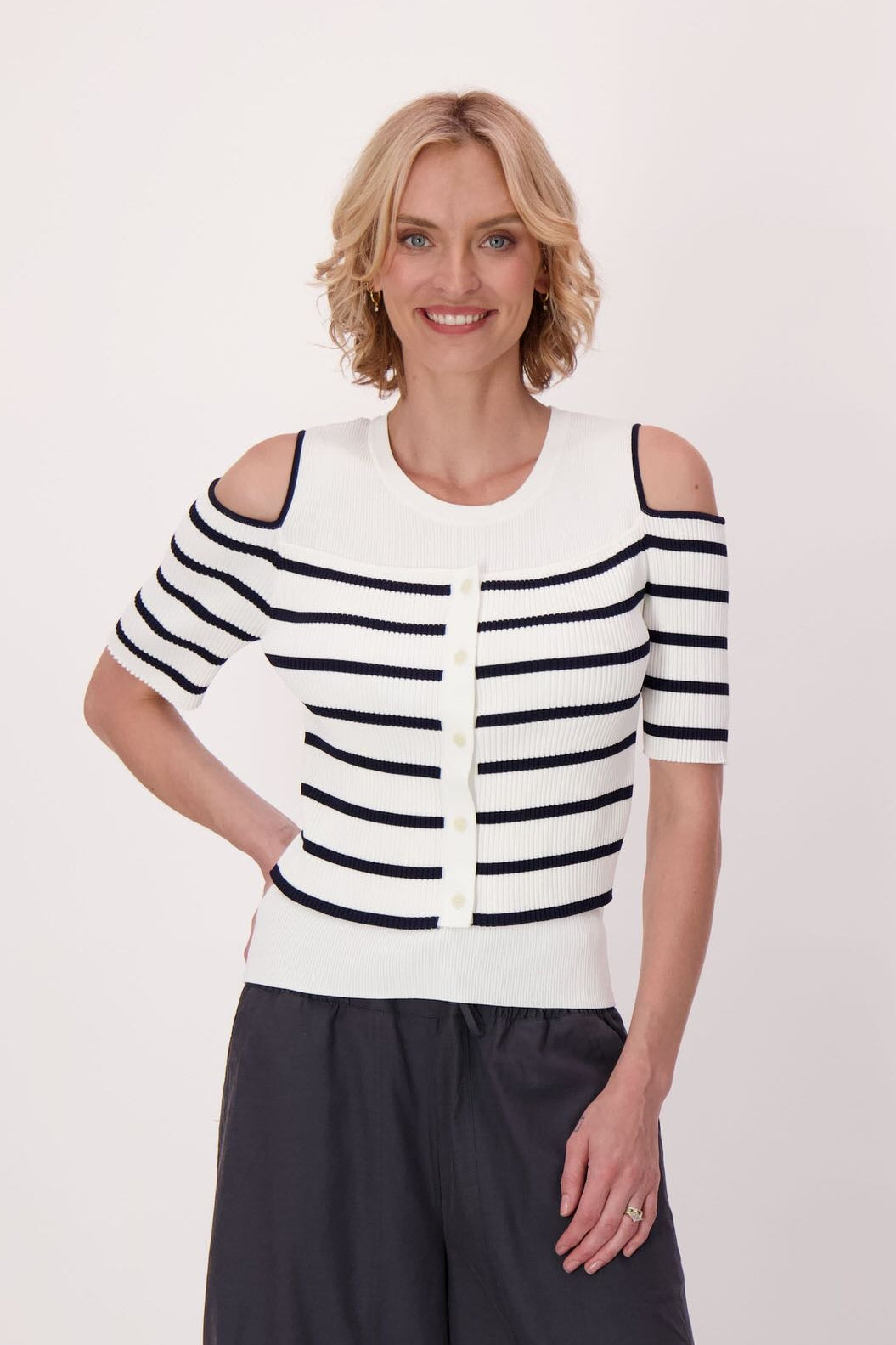 Woman wearing a black and white striped top with cut-out shoulders and black wide-leg pants on a white background