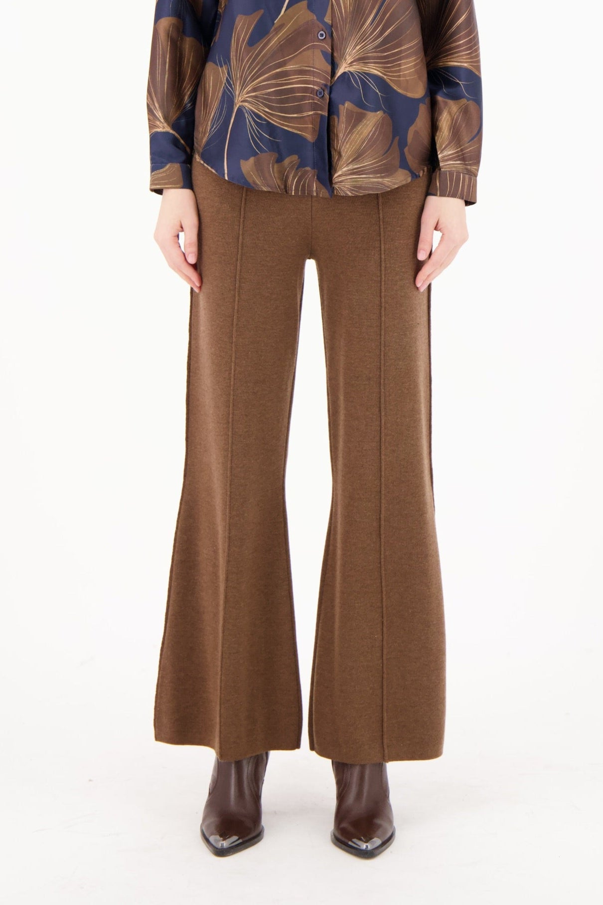 Woman wearing a blue and brown patterned top with brown flared pants on a white background