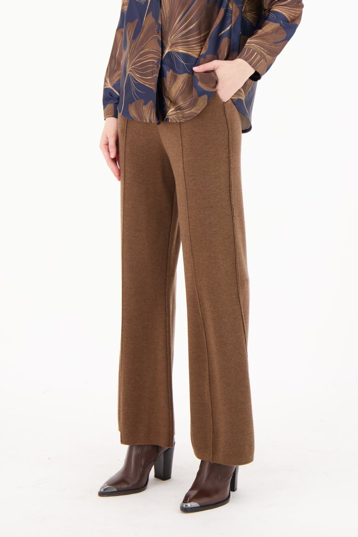 Woman wearing a patterned jacket and brown pants on a white background