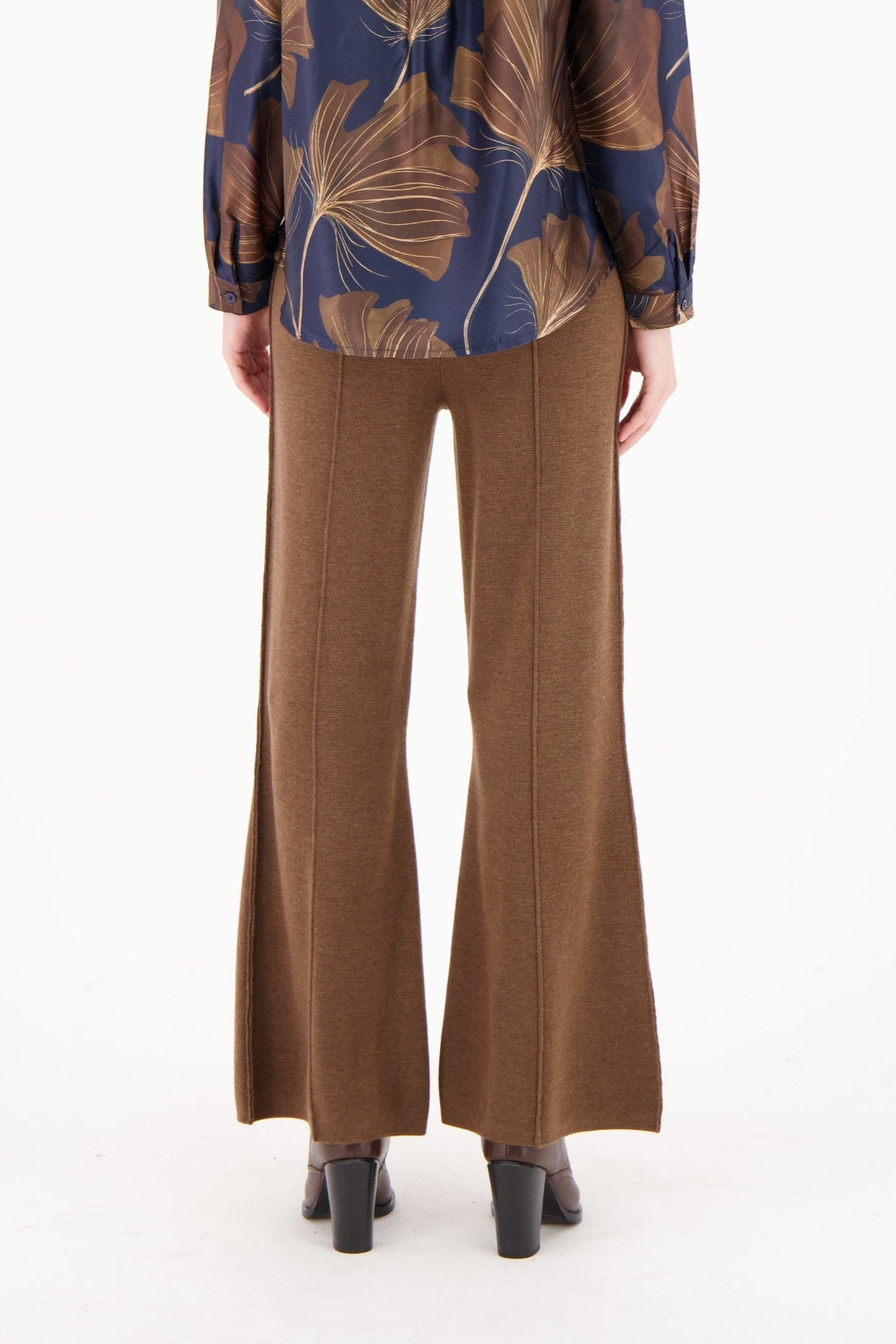 Person wearing a blue blouse with brown leaf patterns and brown pants on a white background