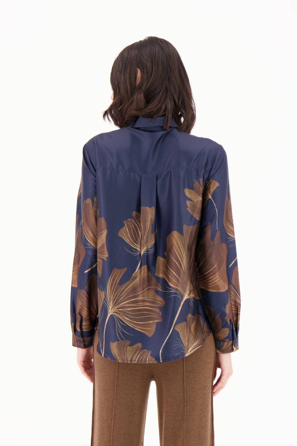 Person wearing a blue blouse with brown leaf patterns and brown pants on a white background