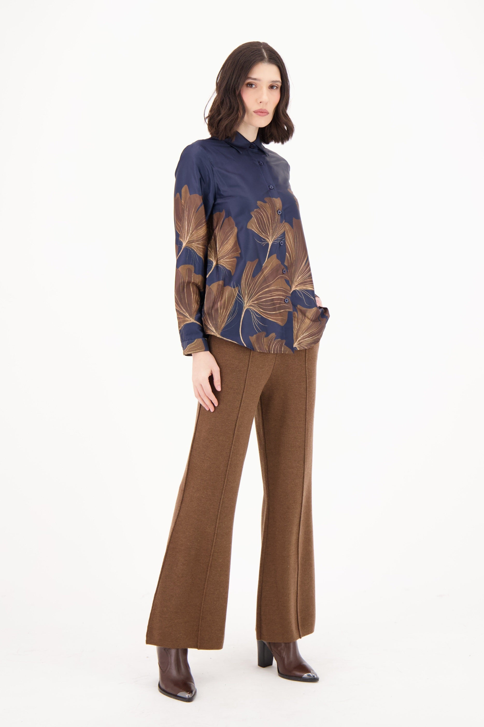 Woman wearing a blue and brown patterned top with brown pants on a white background