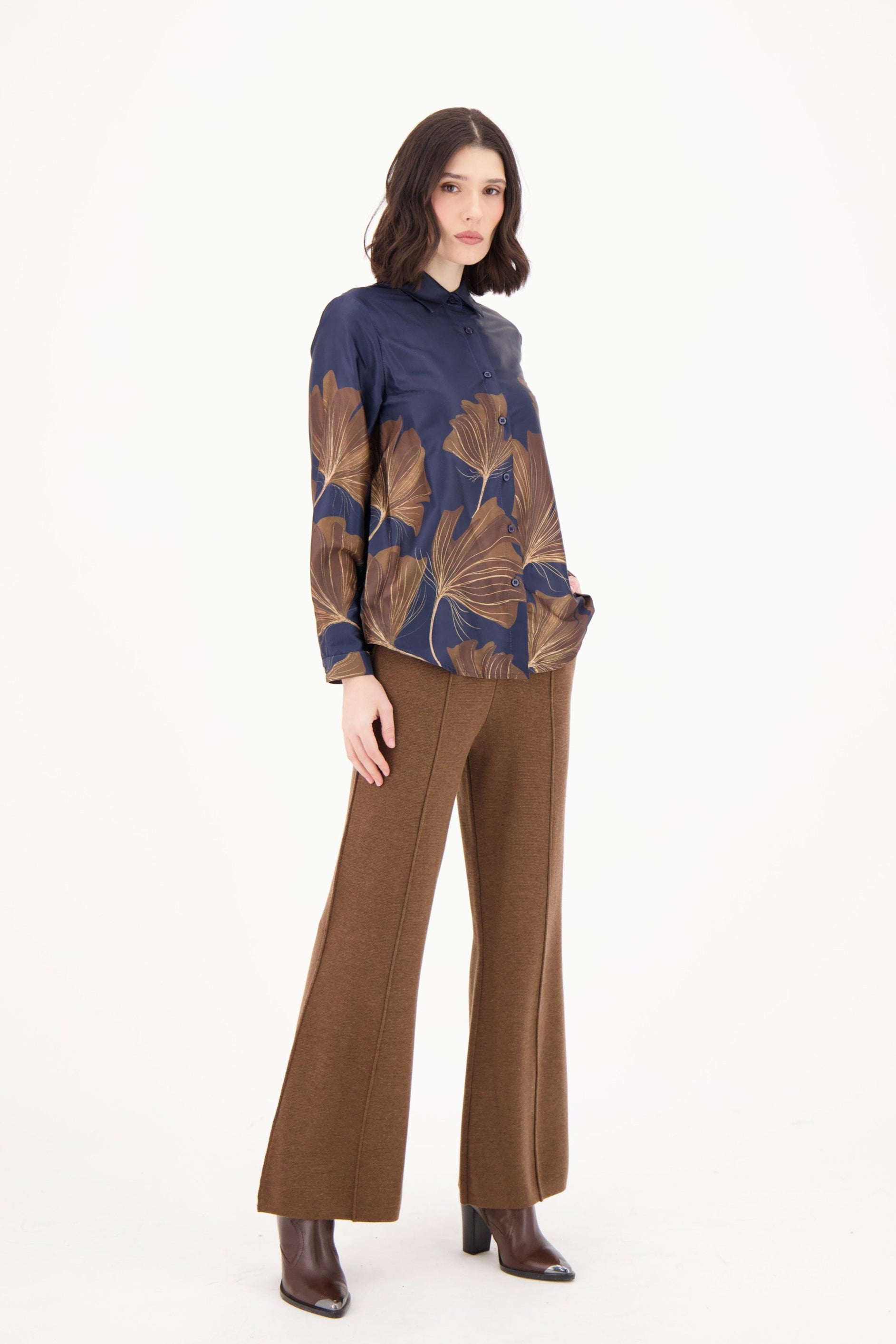 Woman wearing a blue and brown patterned top with brown pants on a white background