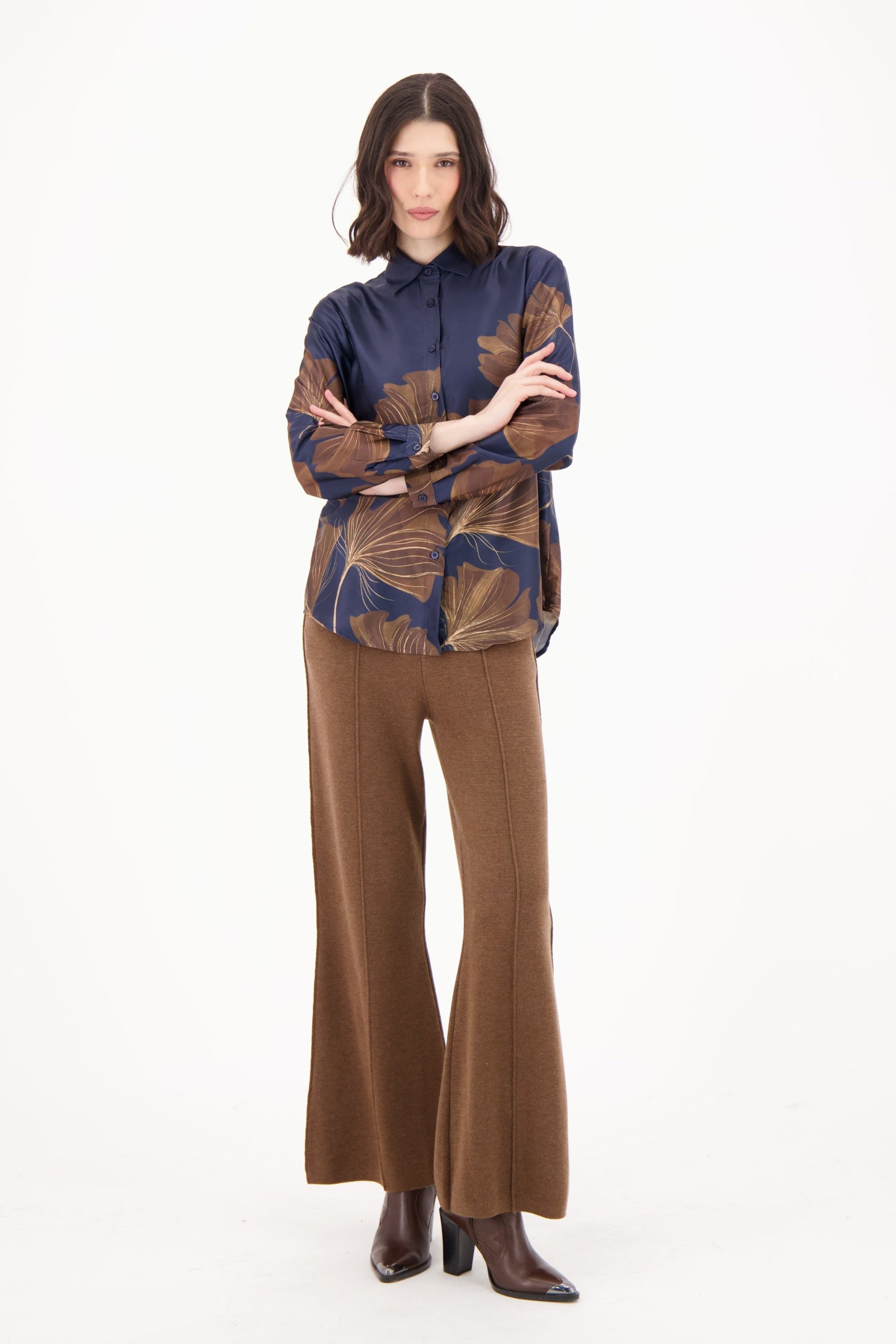 Woman wearing a patterned blouse and brown pants on a white background