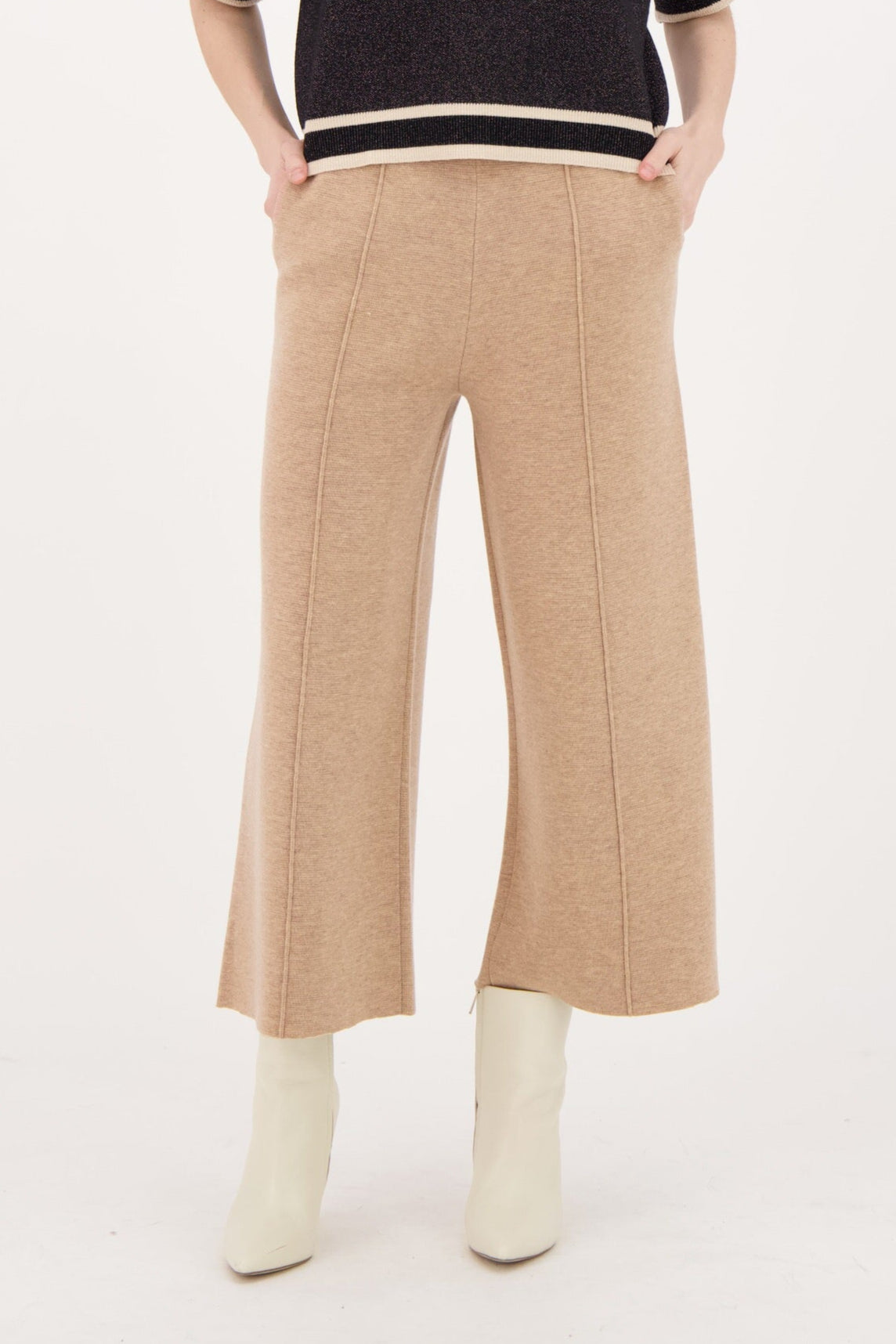 Woman wearing a black sweater with white trim and beige pants on a white background