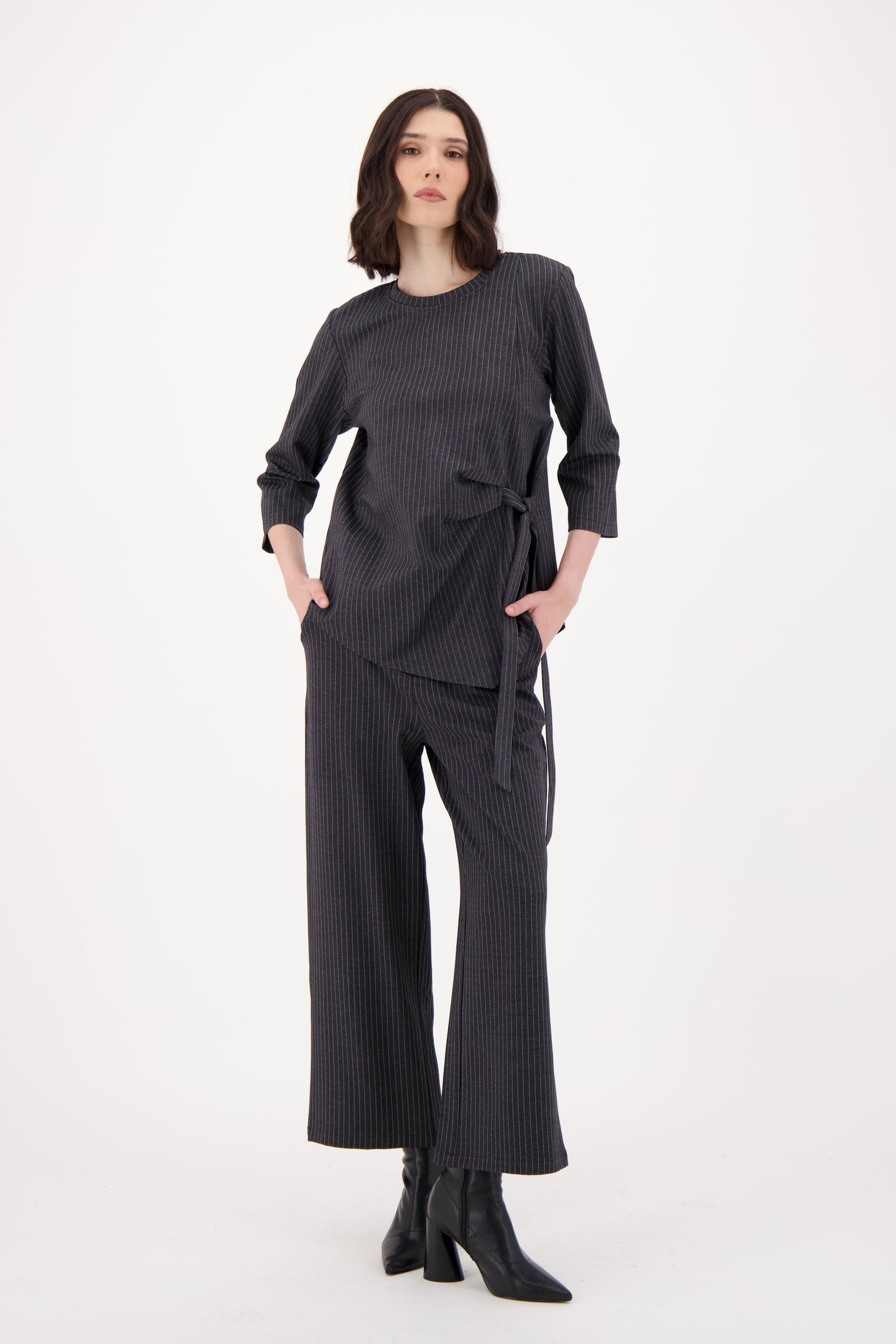 Woman wearing a dark gray outfit with wide-leg pants on a white background