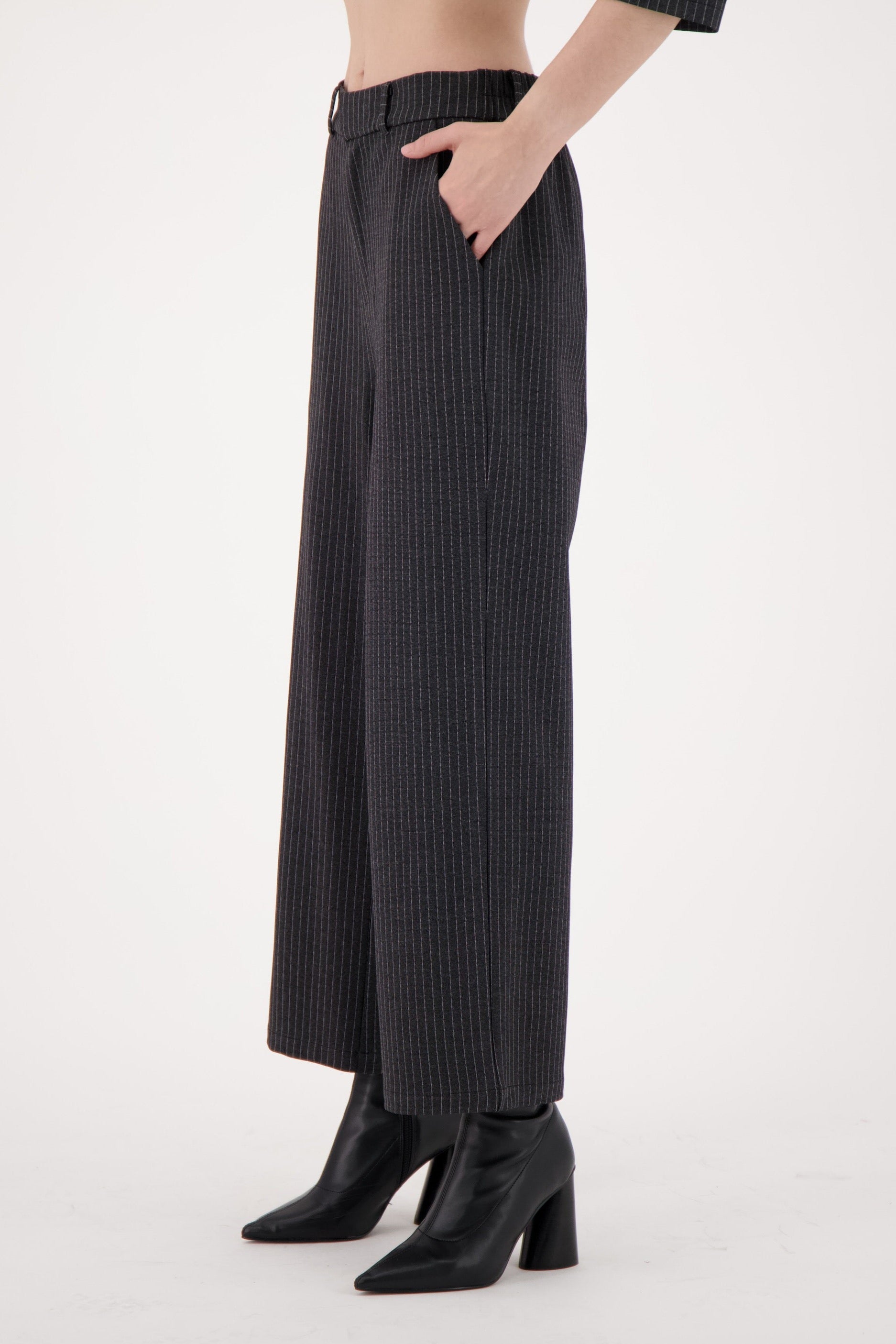 Person wearing black pinstripe pants and black boots on a white background