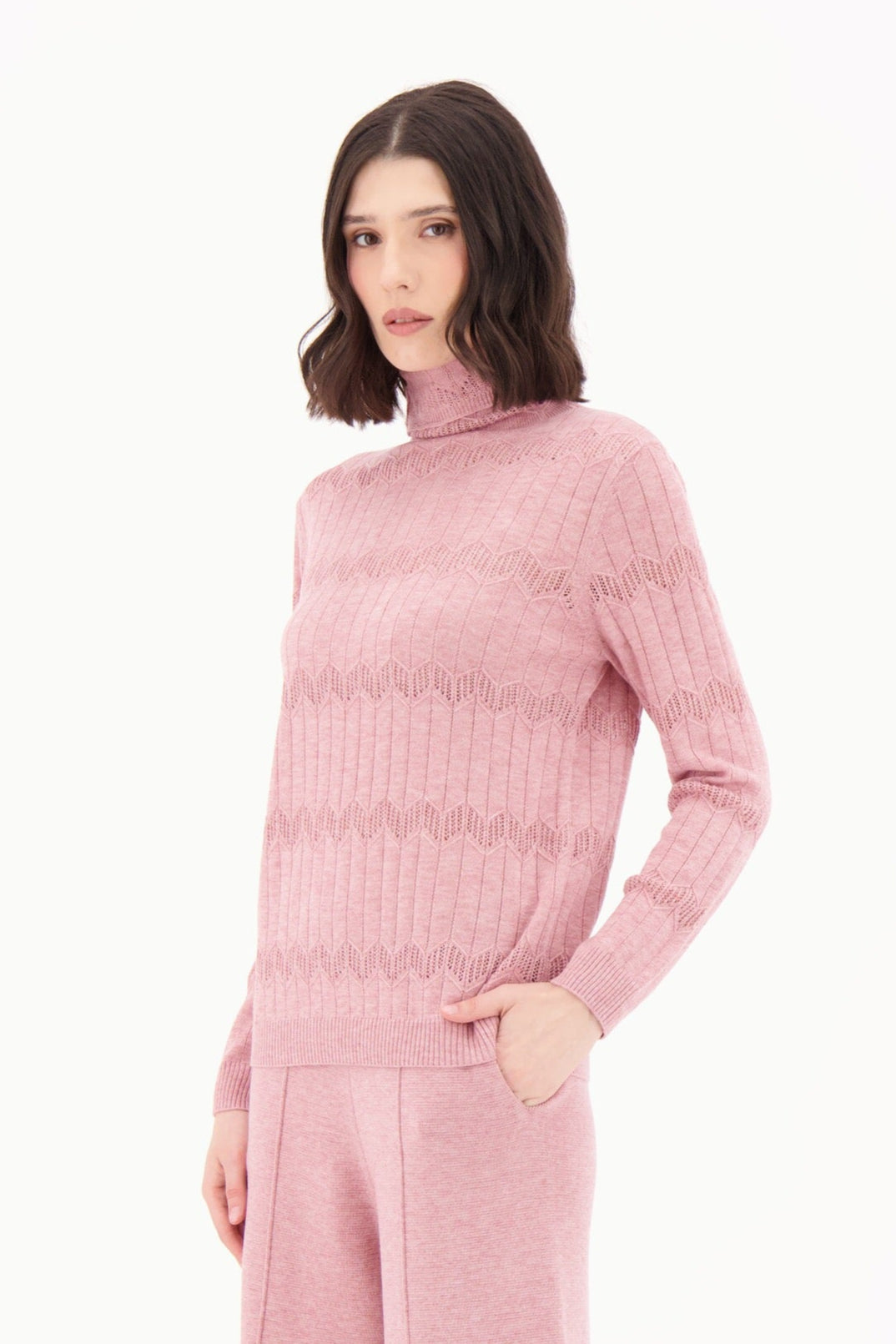 Woman wearing a pink ribbed knit sweater and pants with white boots on a white background