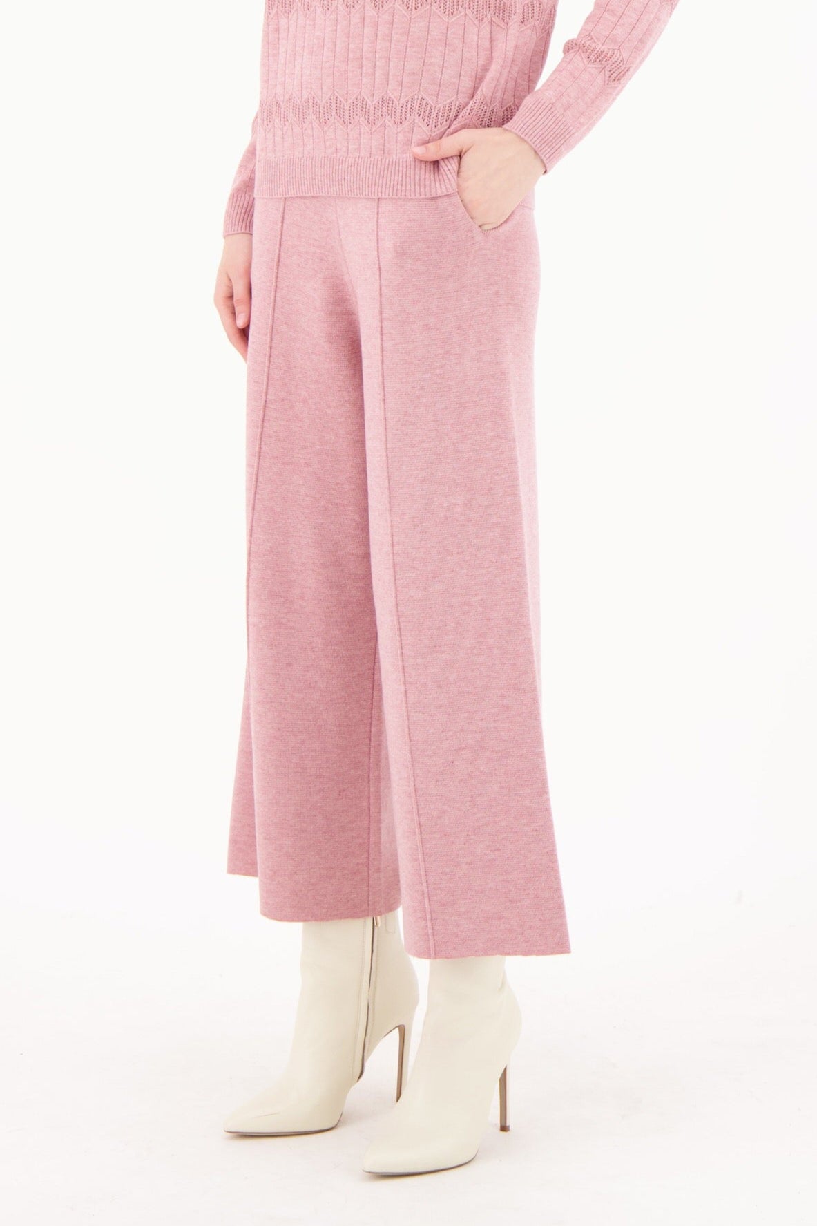 Woman wearing a pink ribbed sweater and pants with white boots on a white background