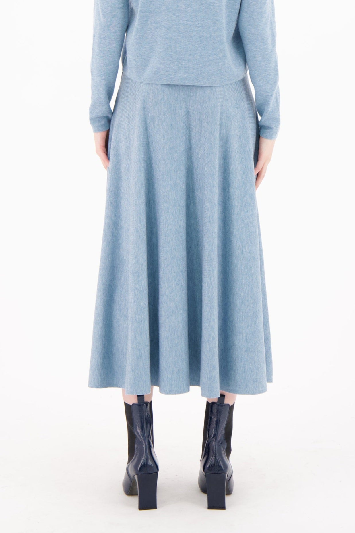 Woman wearing a light blue outfit with a sweater and skirt on a white background