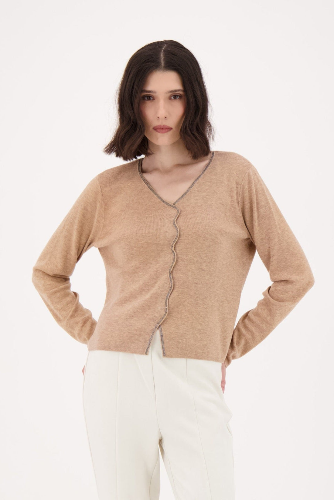 Woman wearing a beige cardigan and white pants on a white background