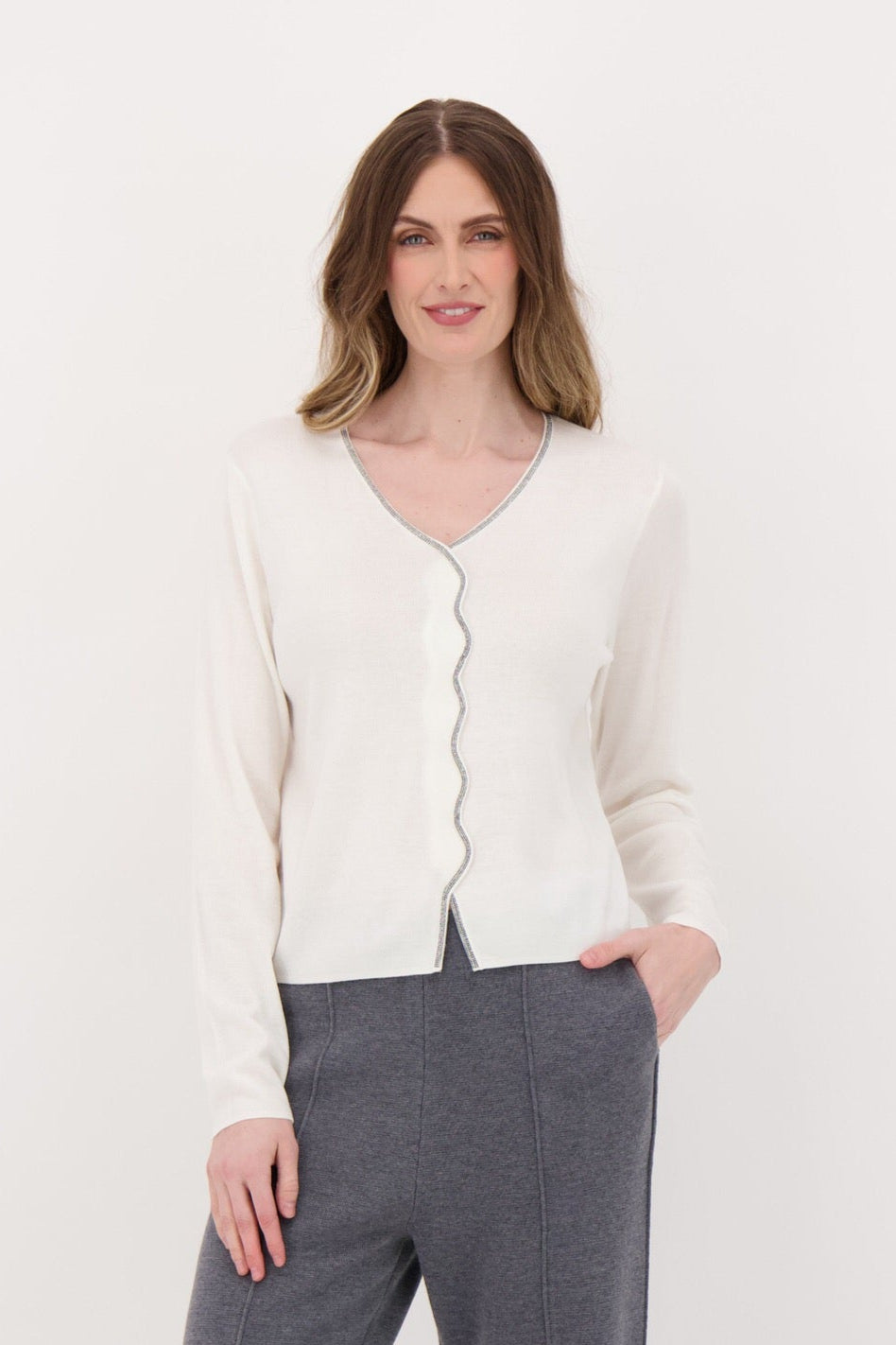 Woman wearing a white cardigan and gray pants on a white background