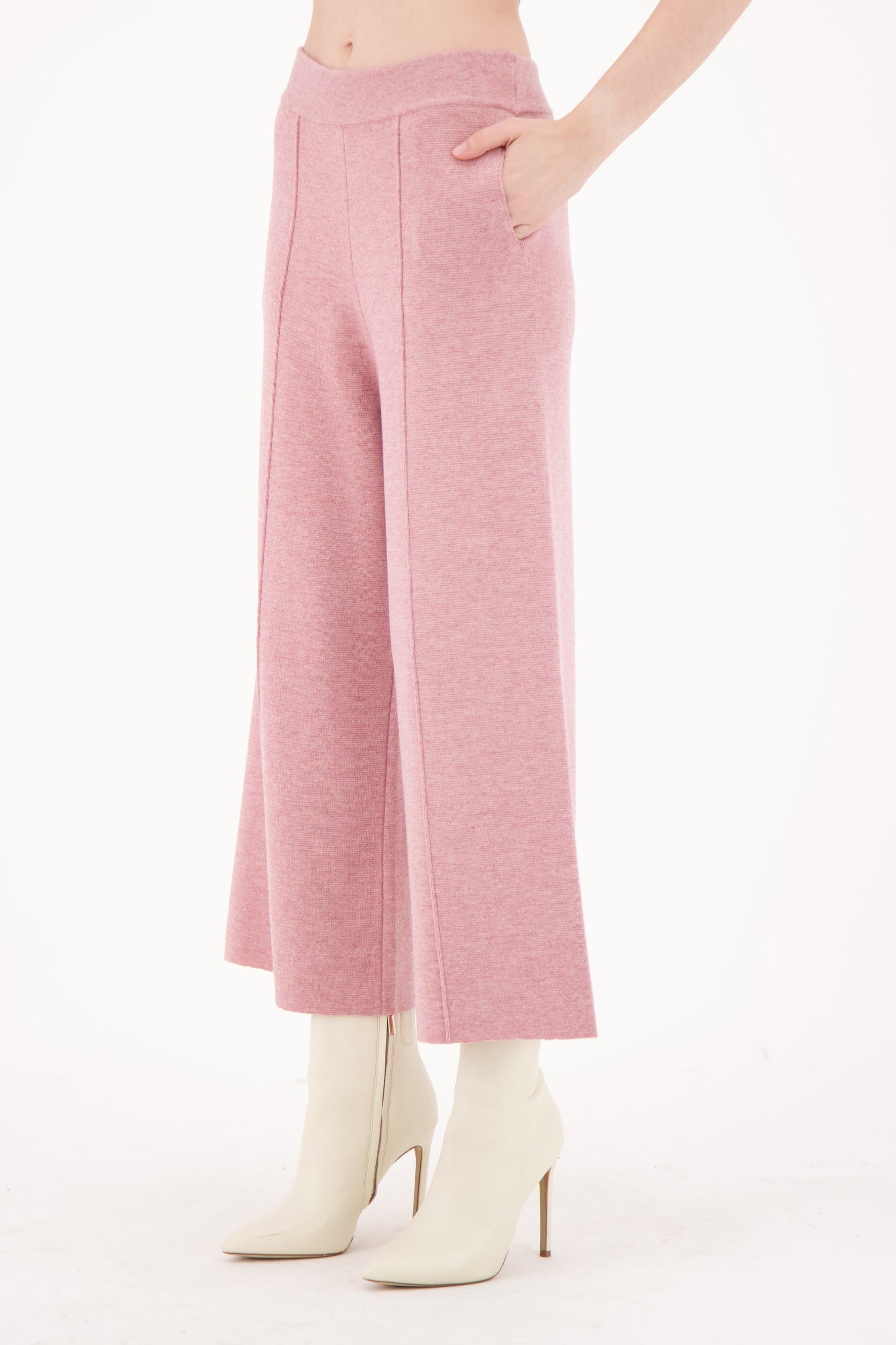 Person wearing pink wide-leg pants and white boots on a light pink background