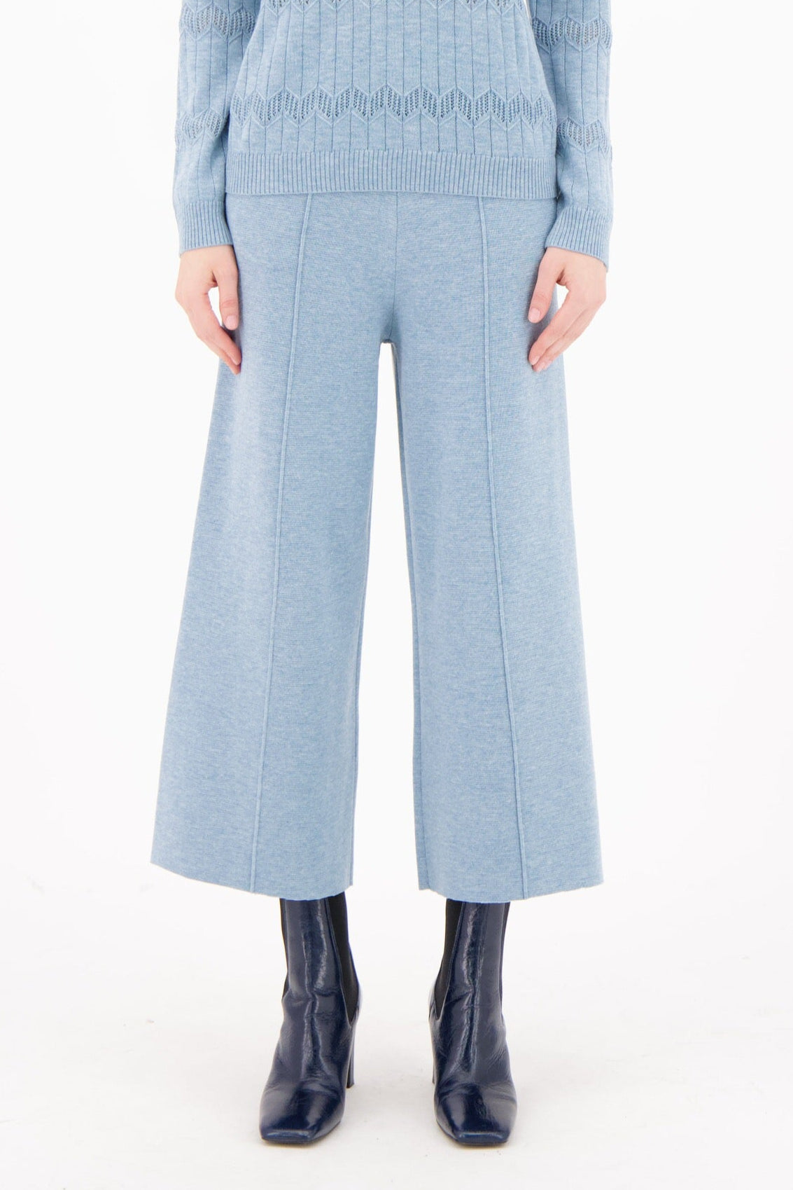 Woman wearing a light blue ribbed sweater and matching pants on a white background