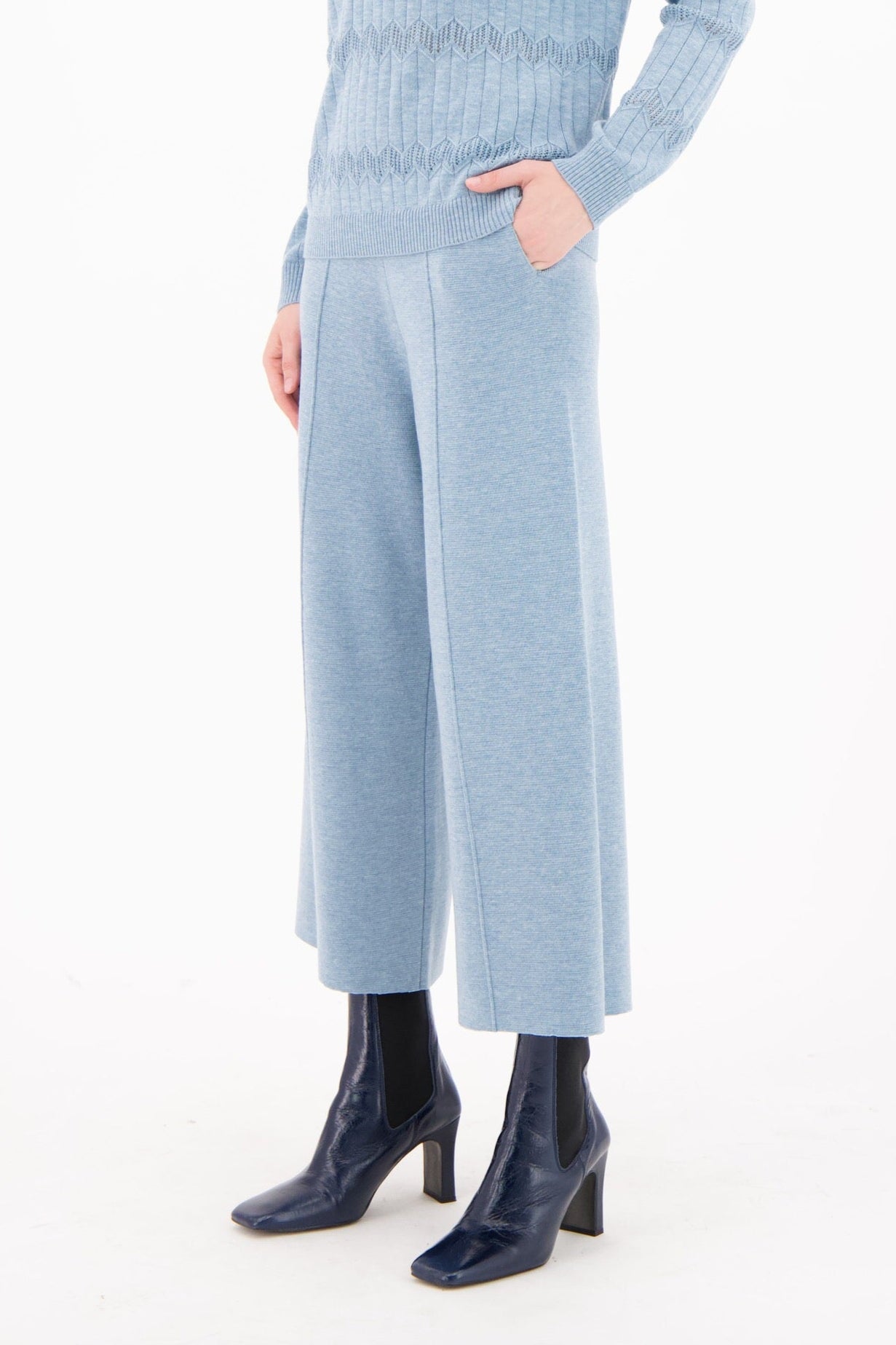 Woman wearing a light blue ribbed sweater and matching pants on a white background