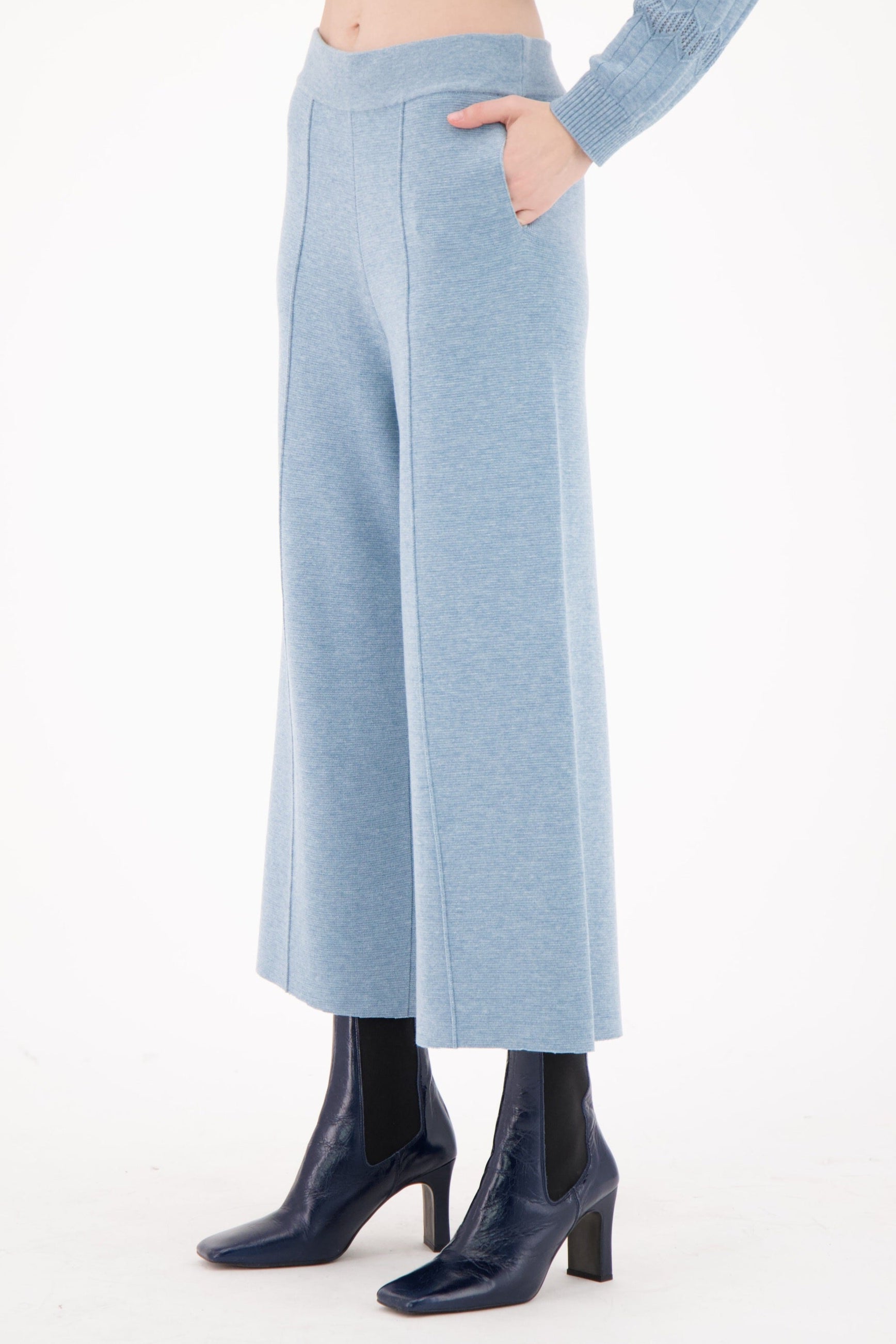 Person wearing light blue ribbed knit pants and dark blue shoes on a white background