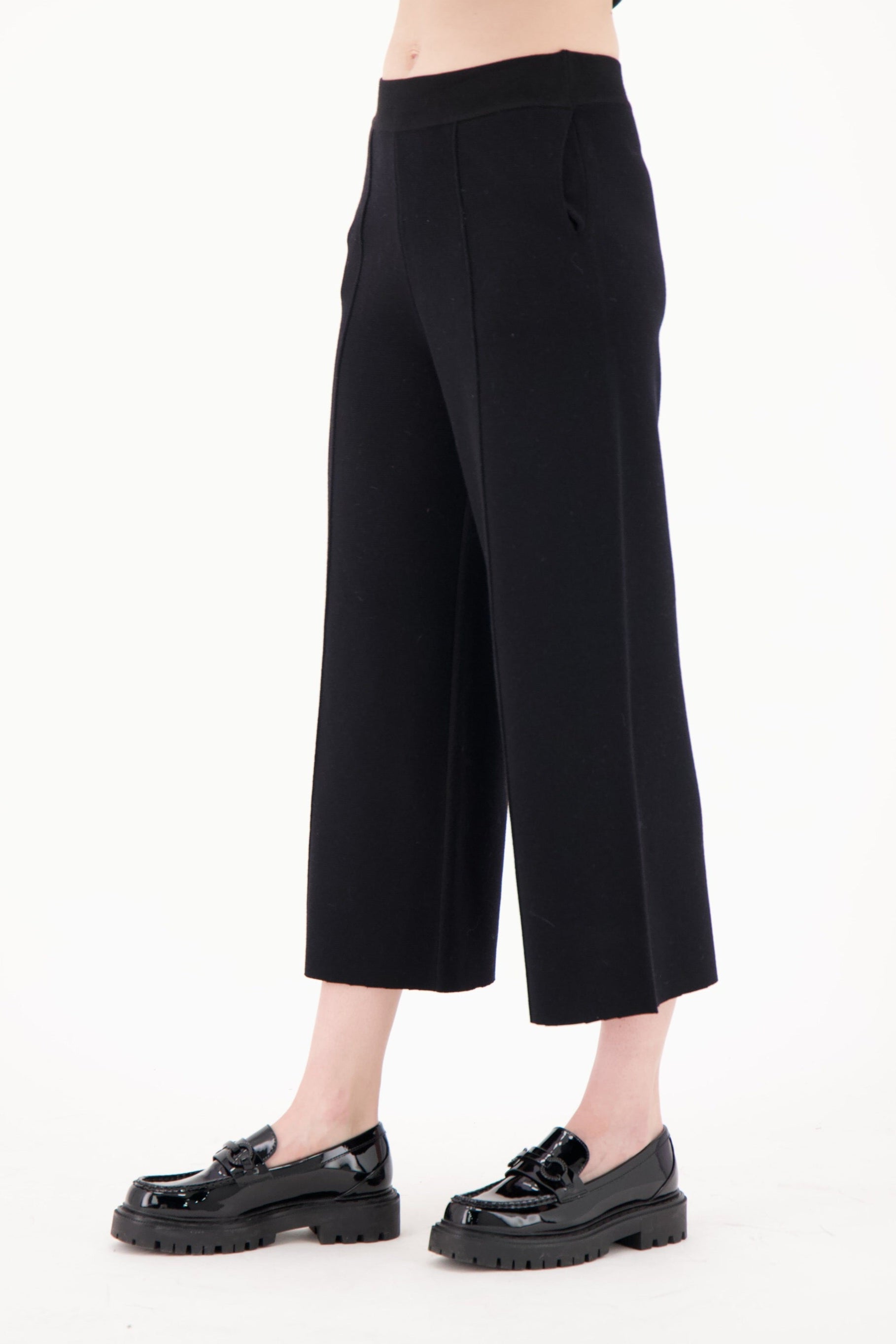 Person wearing black wide-leg pants and black shoes on a white background