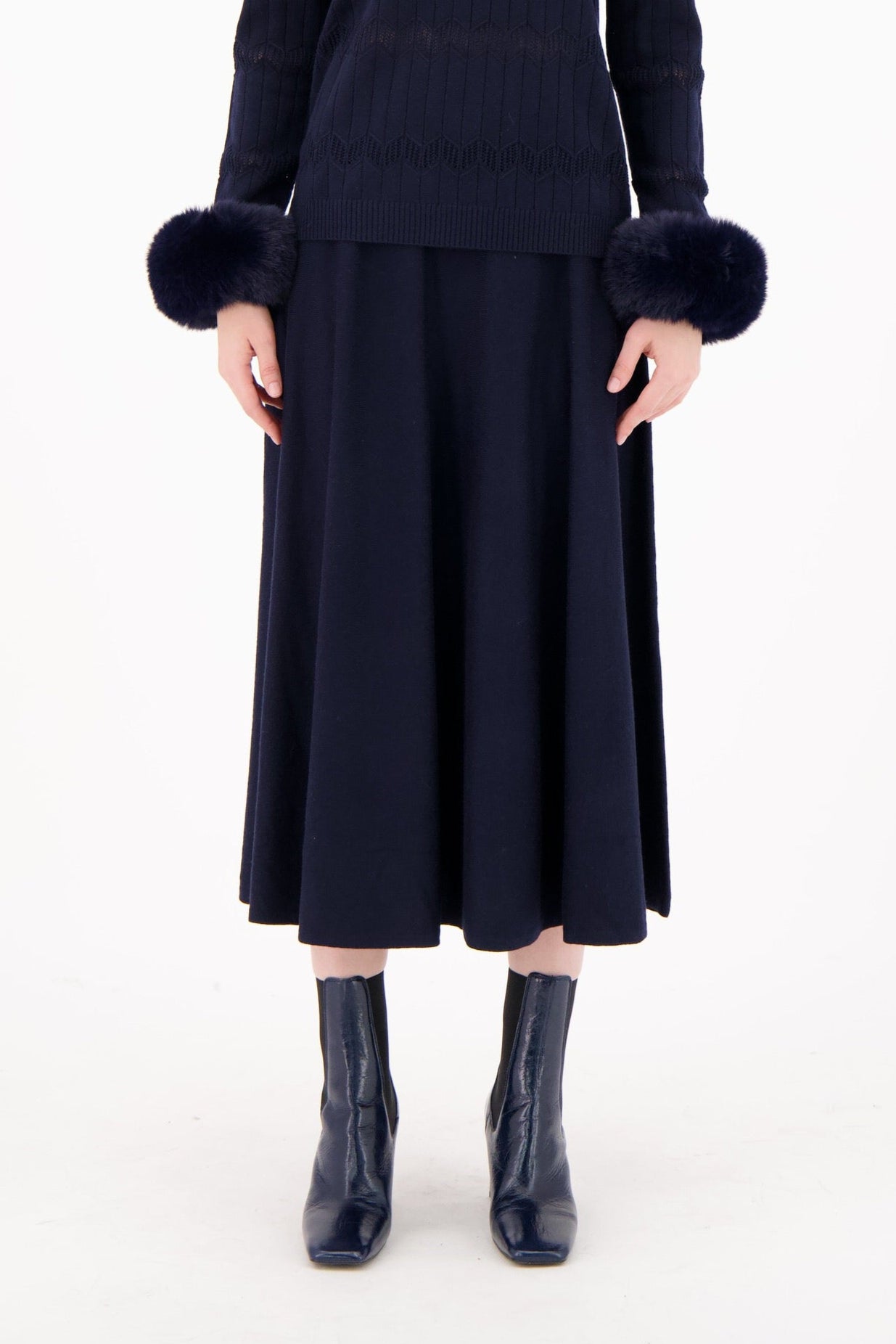 Woman wearing a dark blue dress with fur-trimmed sleeves on a white background