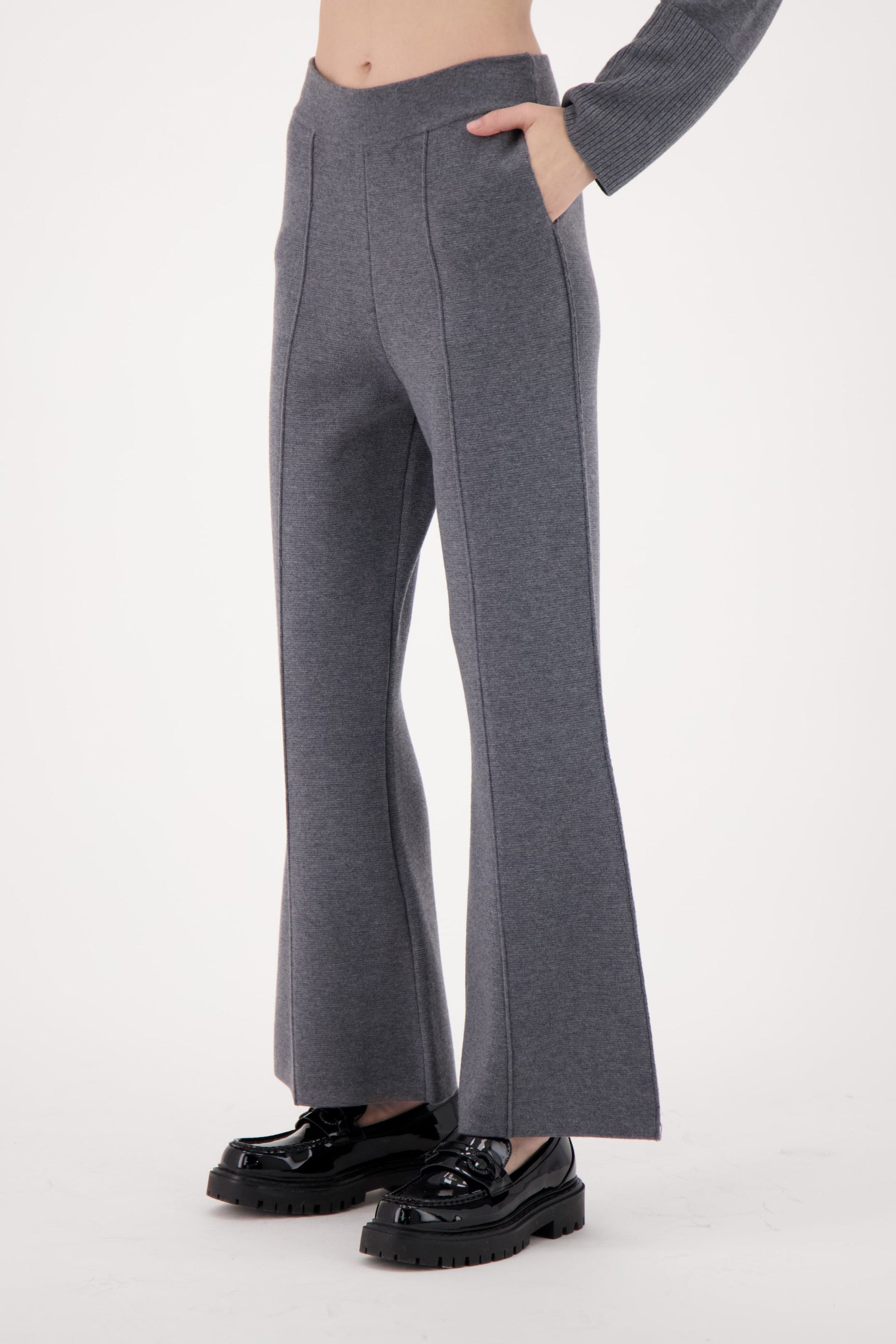 Person wearing gray flared pants and black shoes on a white background