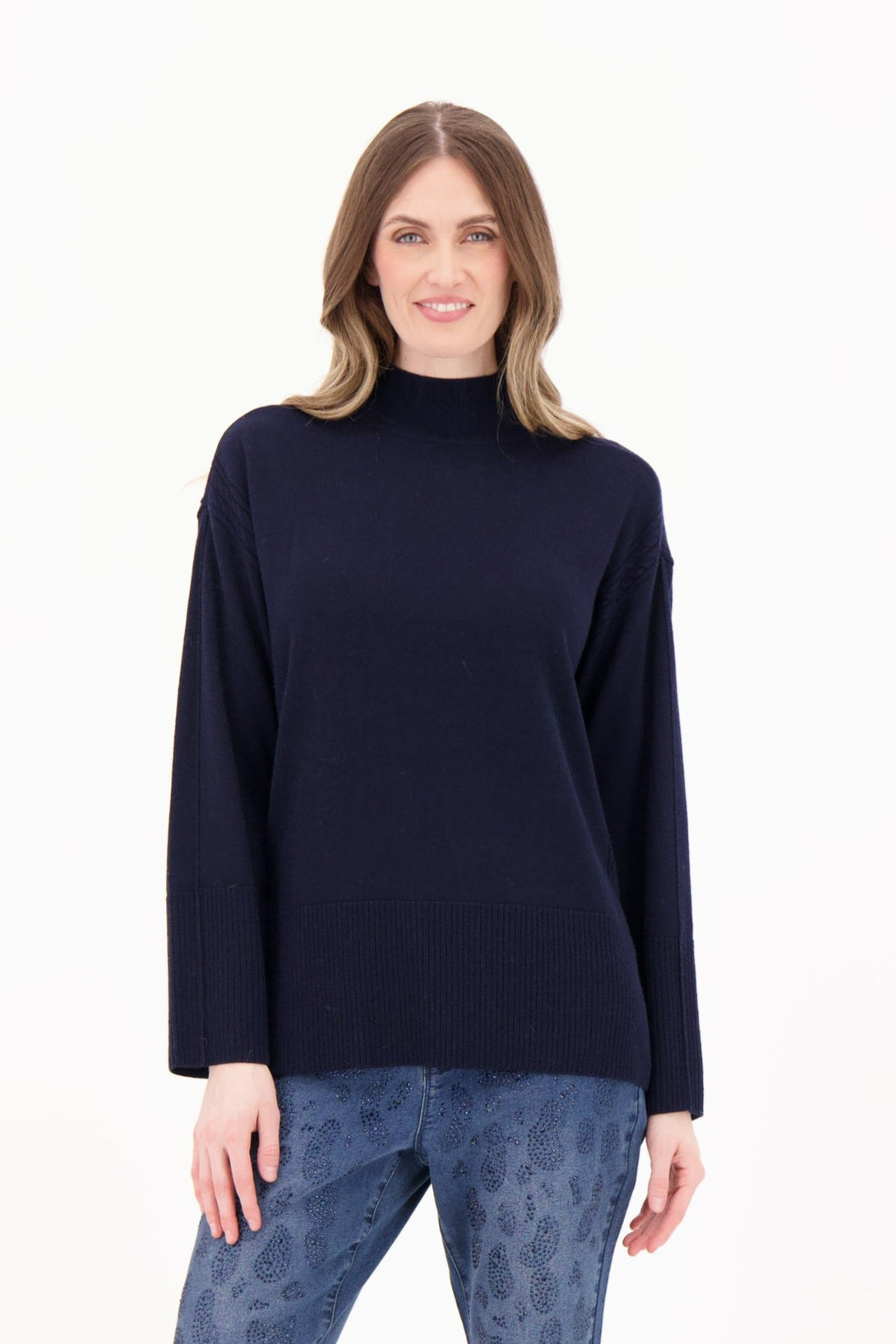 Woman wearing a navy sweater, blue patterned pants, and black boots on a white background