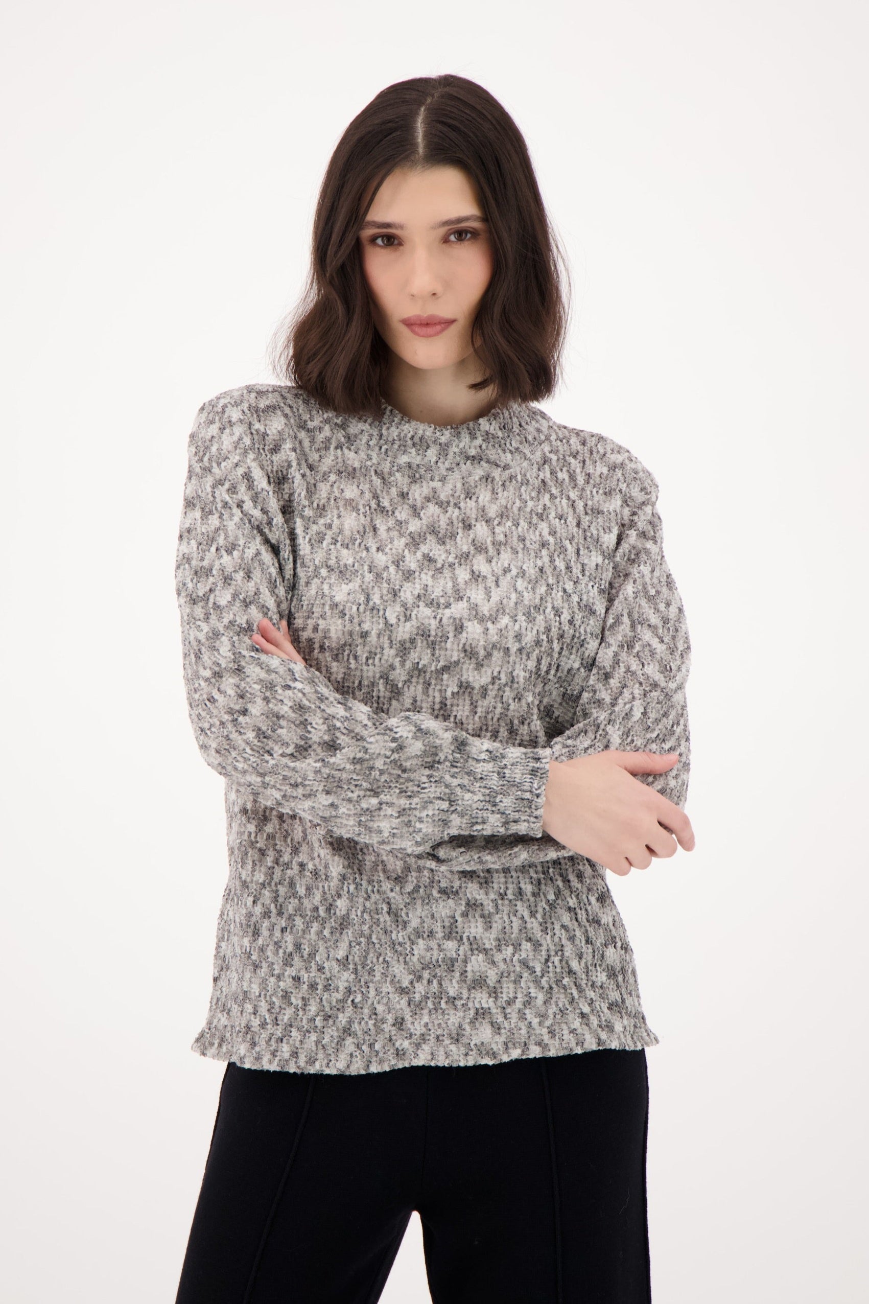 Woman wearing a patterned sweater and black pants on a white background