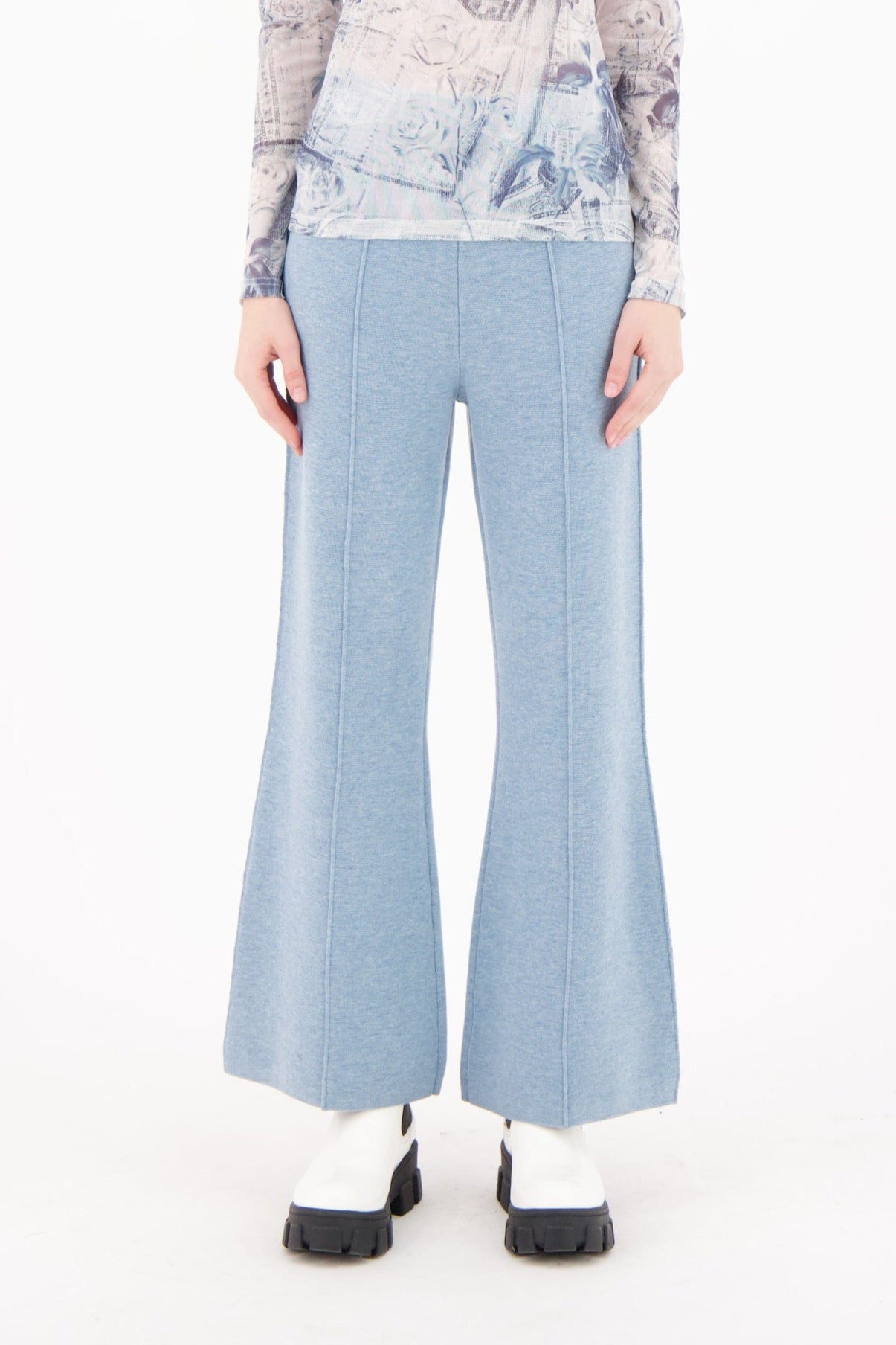 Woman wearing a patterned top and light blue flared pants on a white background