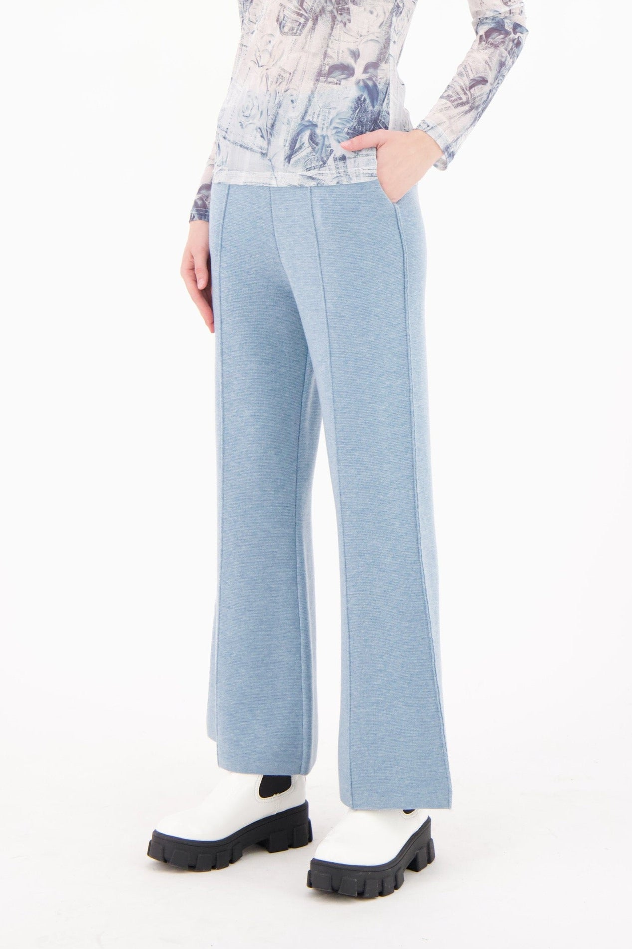 Woman wearing a floral blouse and light blue pants on a white background