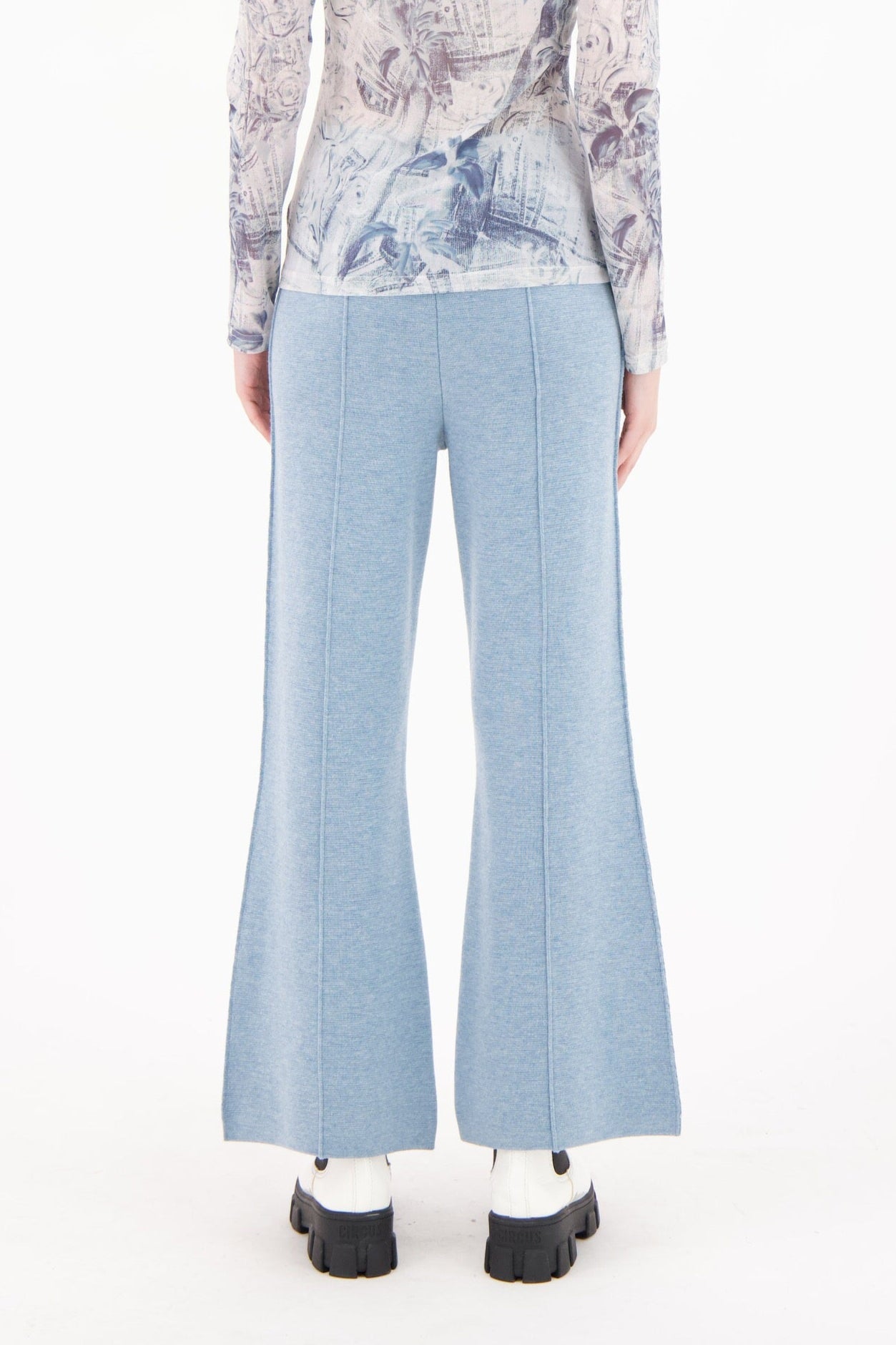 Person wearing a floral blouse and light blue pants on a white background