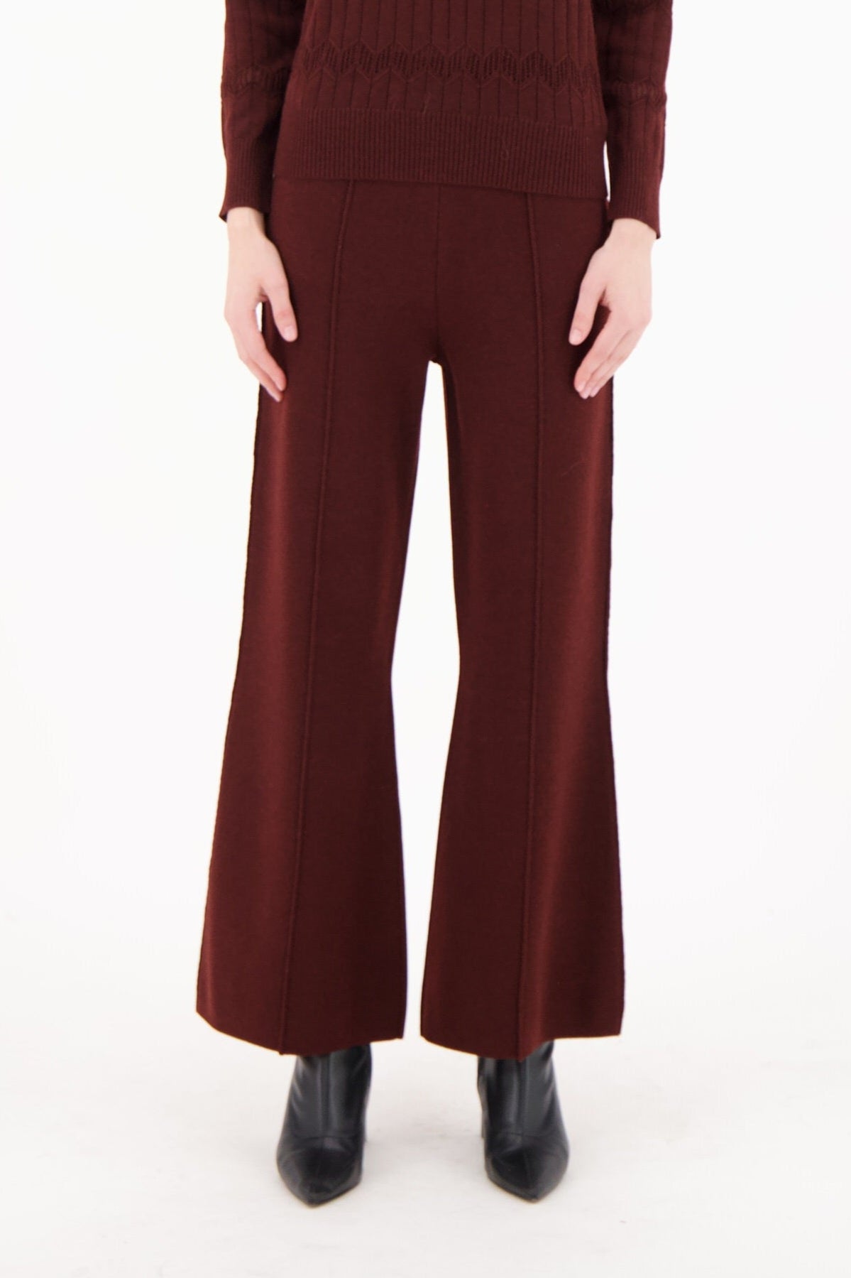 Woman wearing a burgundy sweater and flared pants on a white background