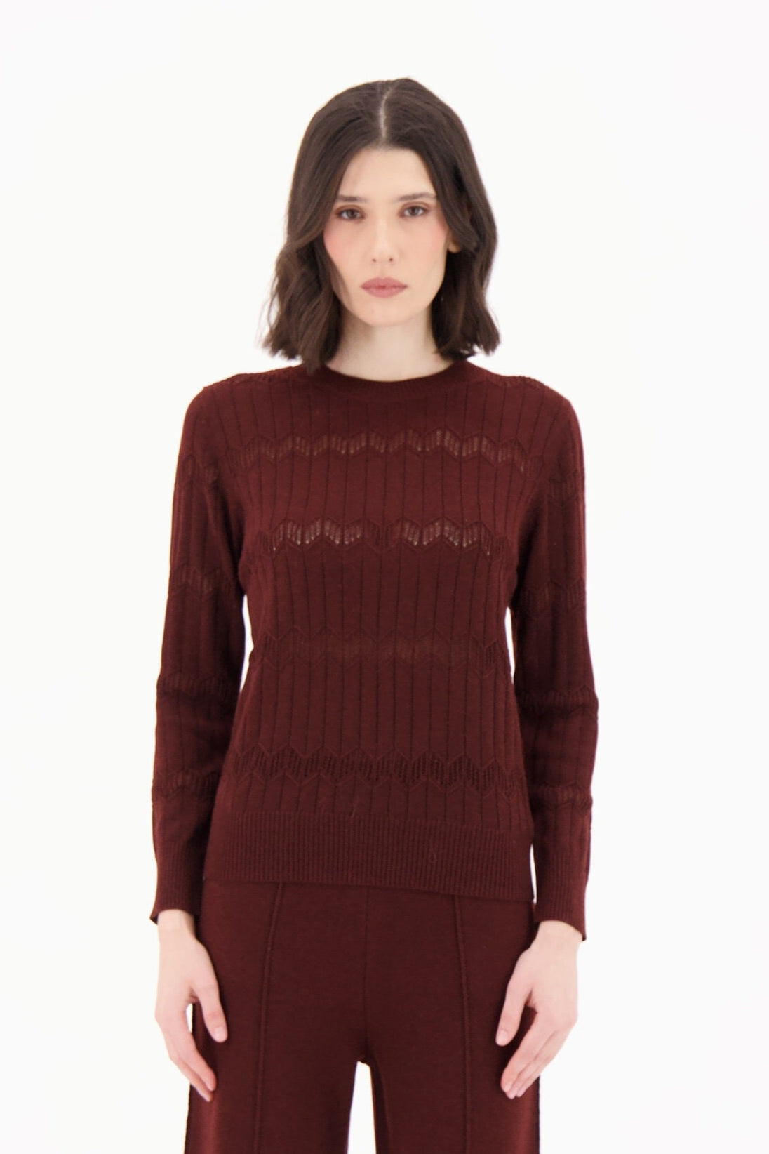 Woman wearing a burgundy sweater and flared pants on a white background