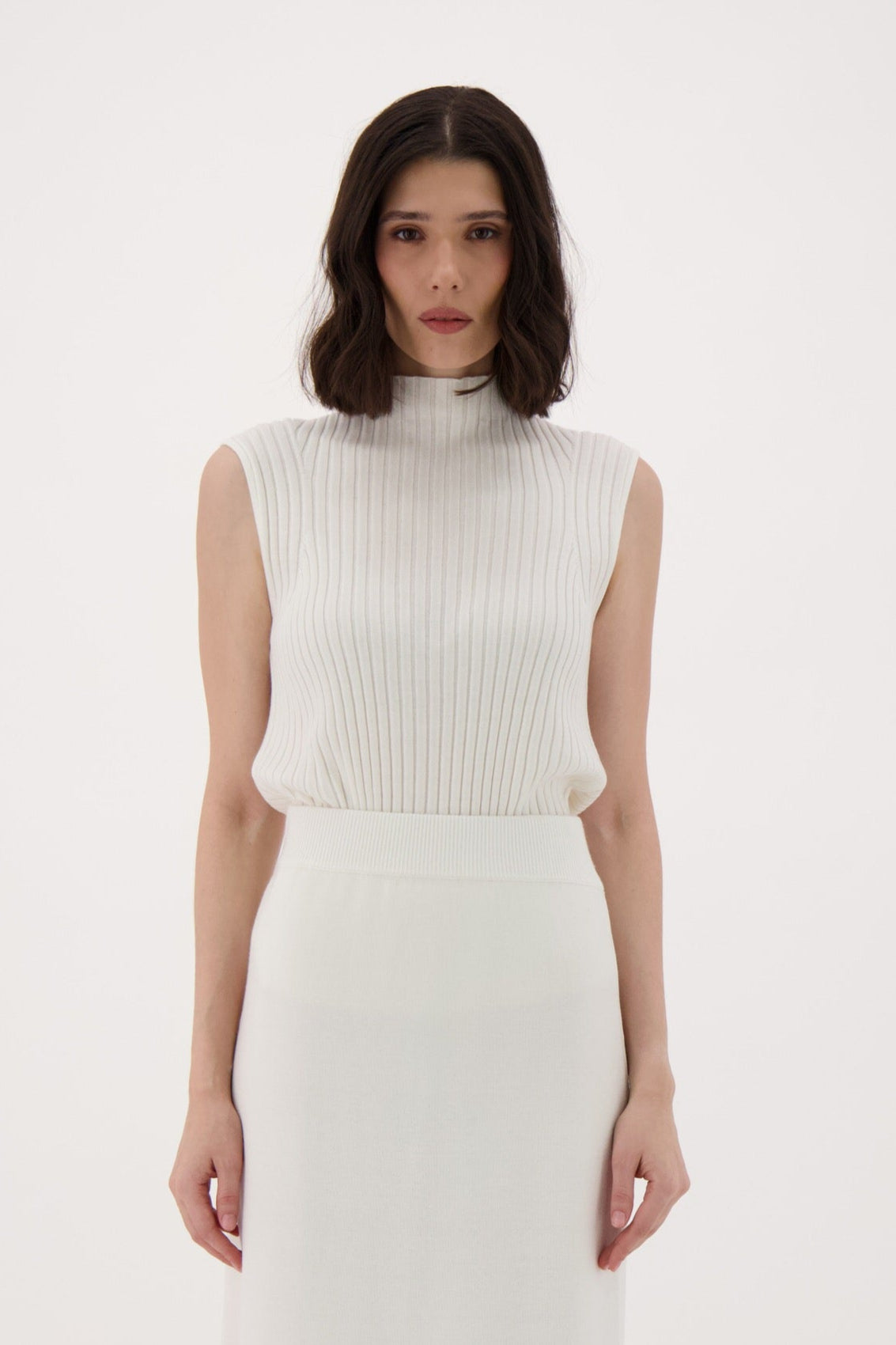 Woman wearing a white sleeveless top and skirt with brown boots on a white background