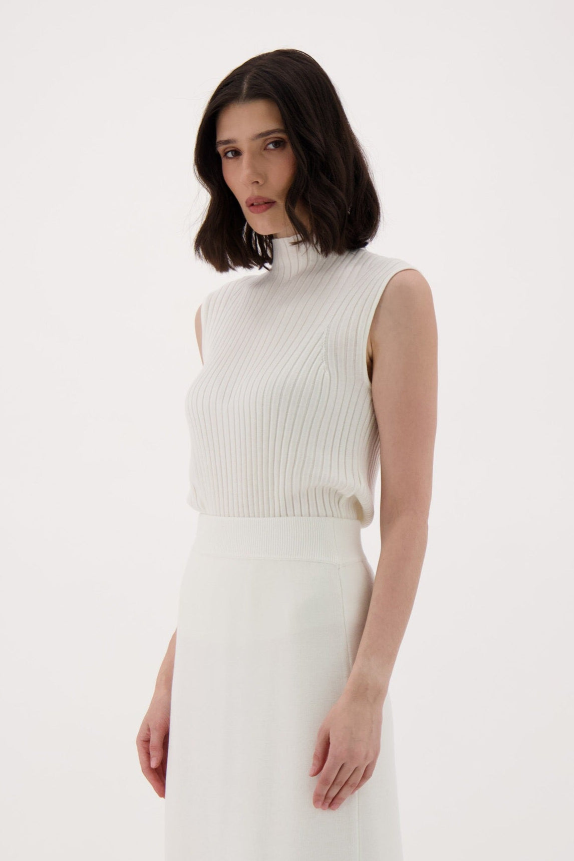 Woman wearing a white sleeveless top and skirt with brown knee-high boots on a white background