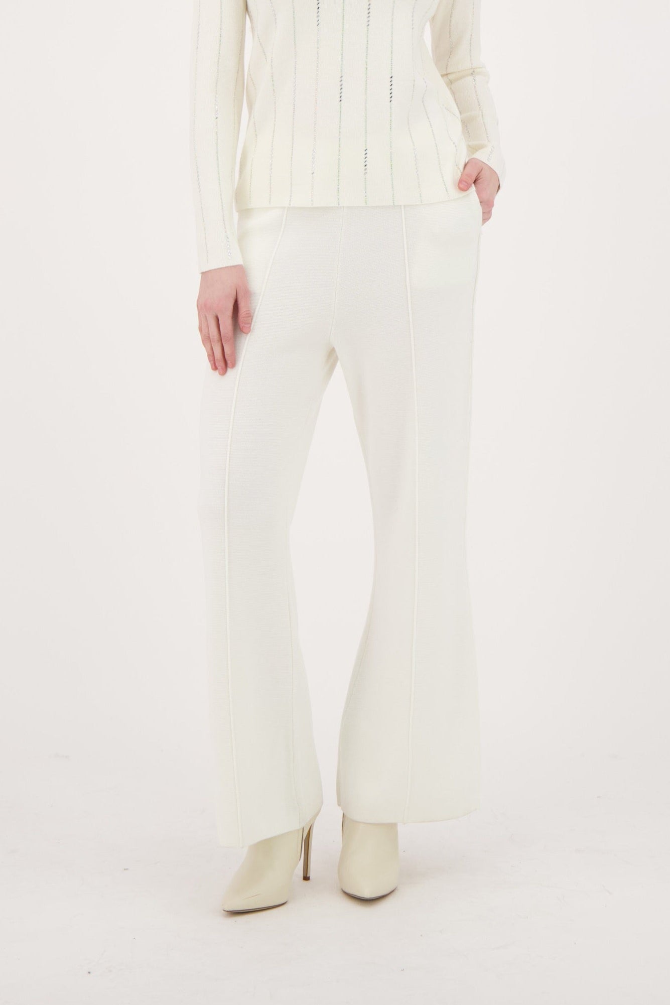 Woman wearing a white cable knit sweater and pants on a white background