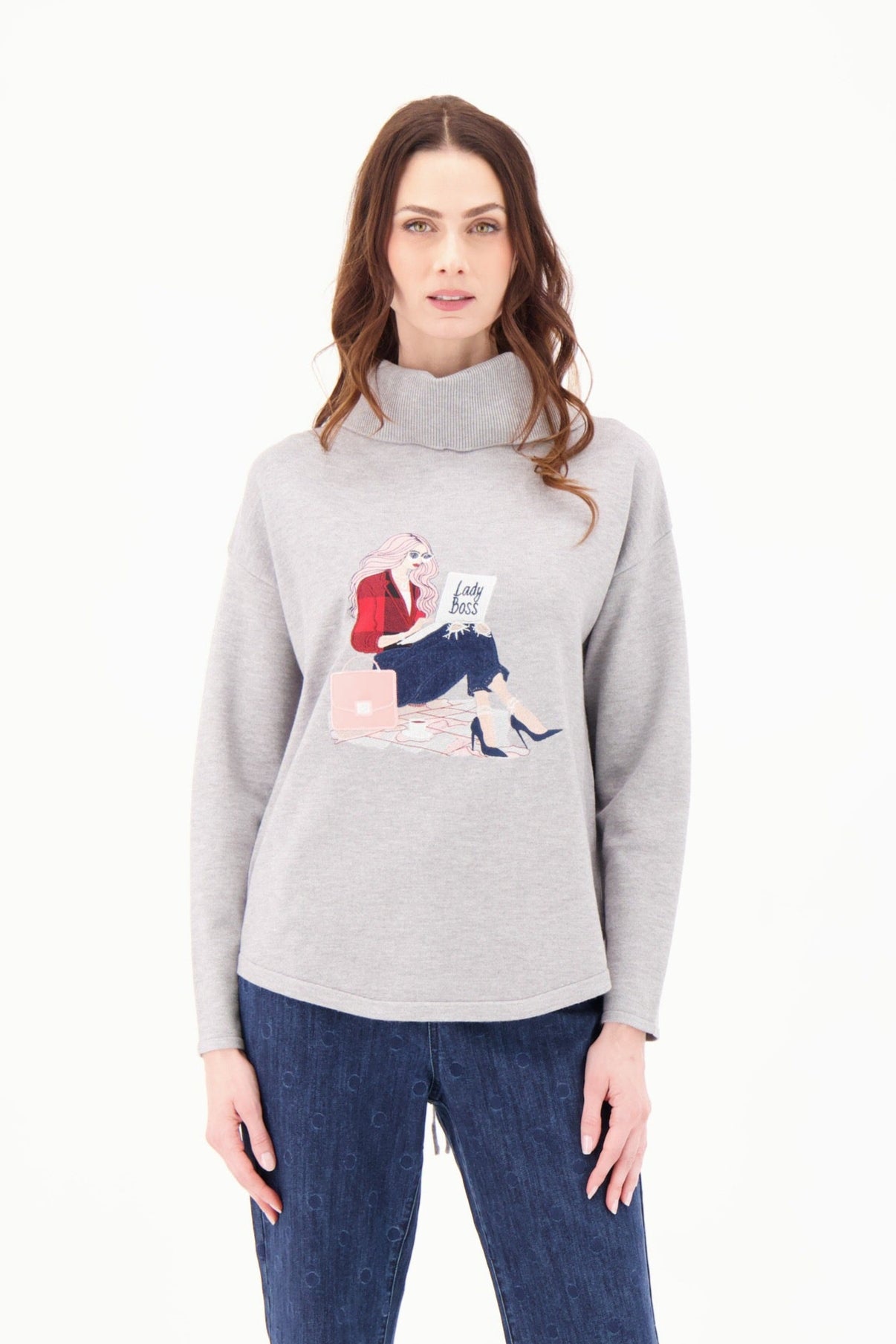 Woman wearing a gray sweater with a graphic design and blue jeans on a white background