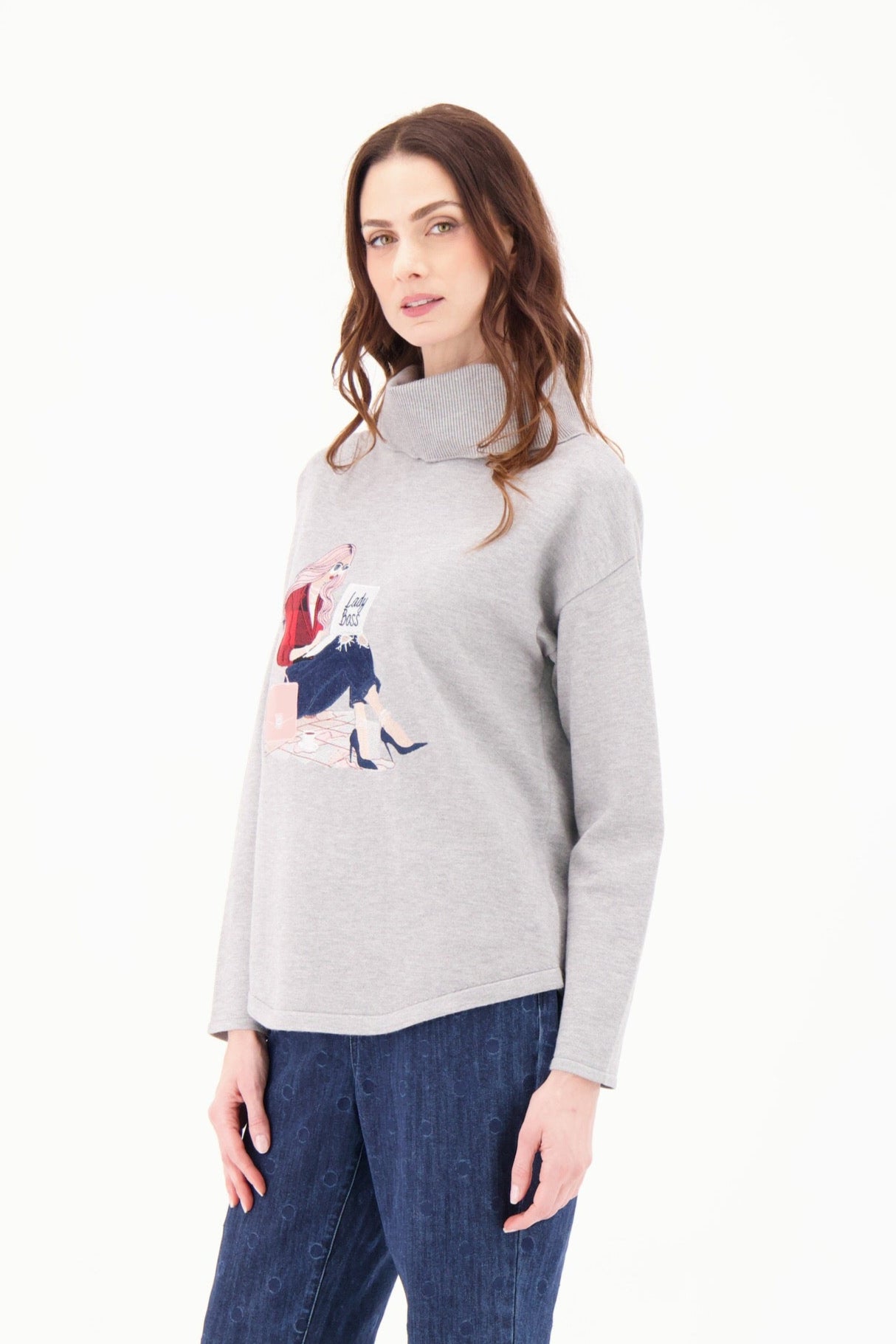 Woman wearing a gray sweater with a graphic design and blue jeans on a white background