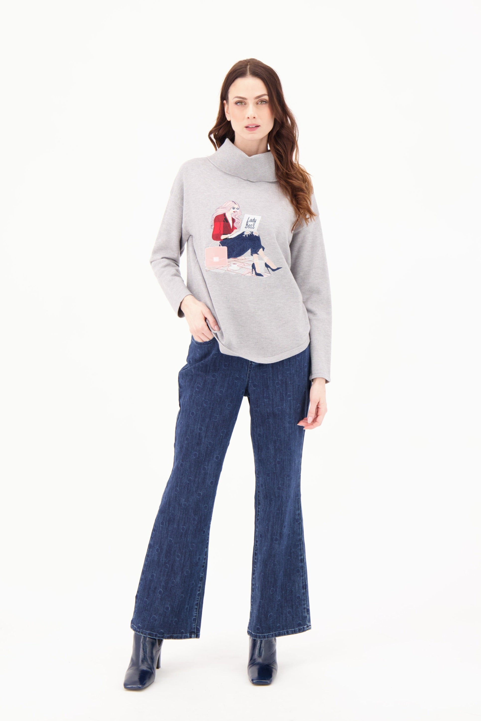 Woman wearing a gray sweater with a colorful design and blue jeans on a white background