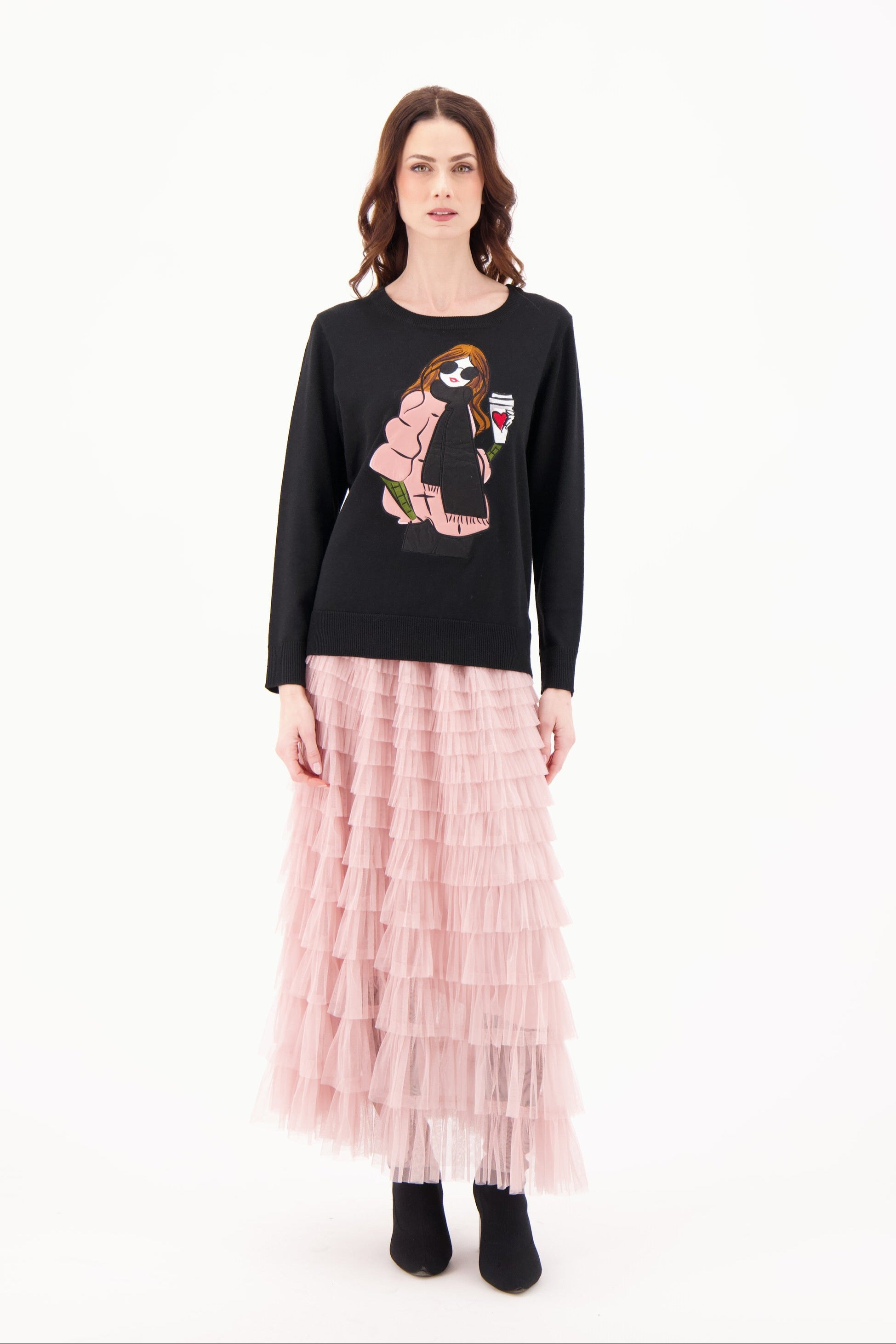 Woman wearing a black sweater with a graphic design and a pink pleated skirt on a white background