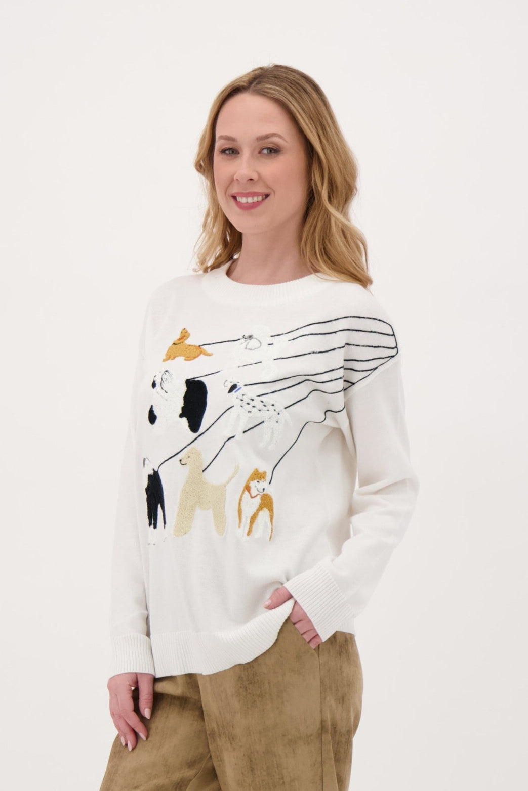 Woman wearing a white sweater with a graphic design and brown pants on a white background
