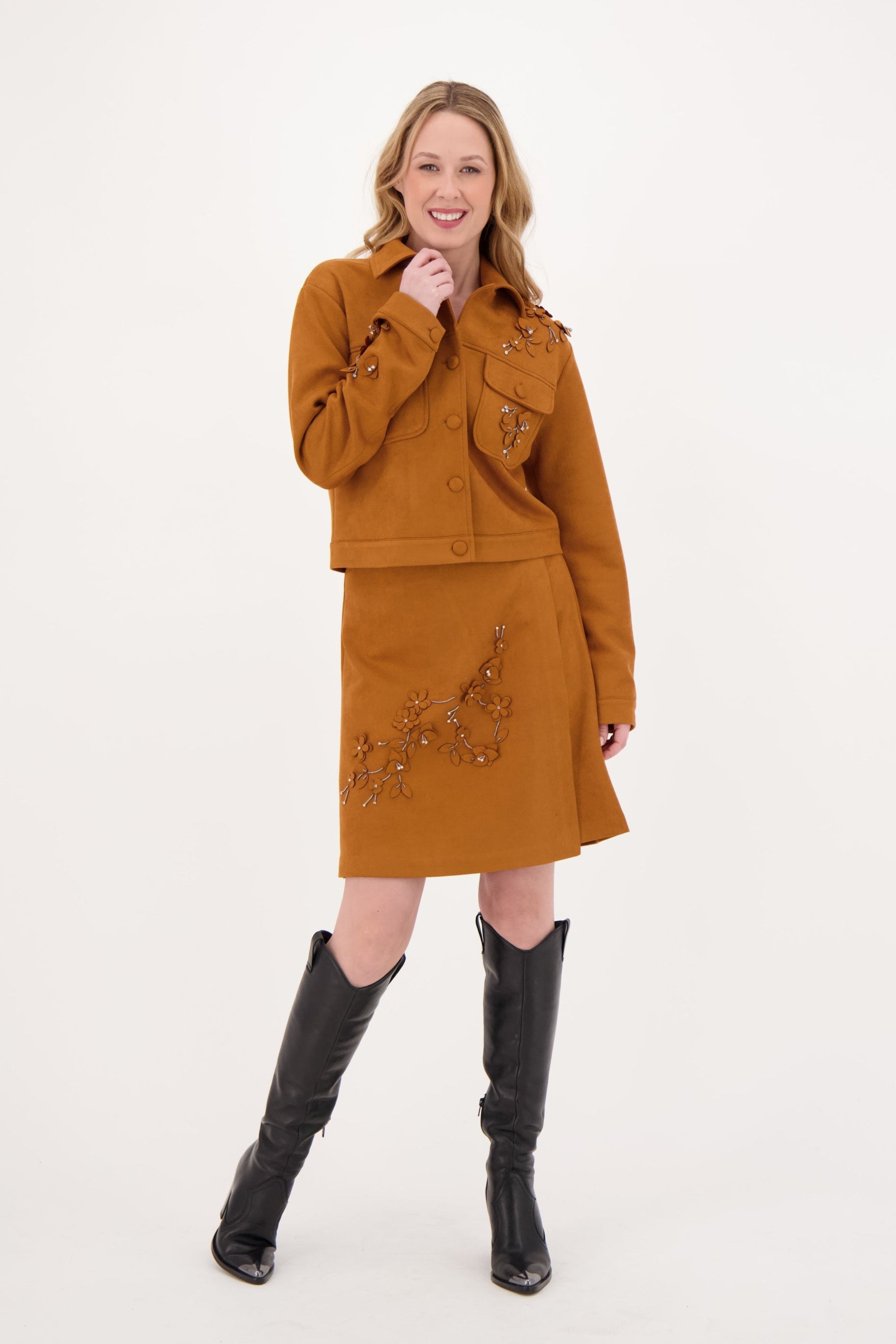 Woman wearing a mustard yellow outfit with black boots on a white background