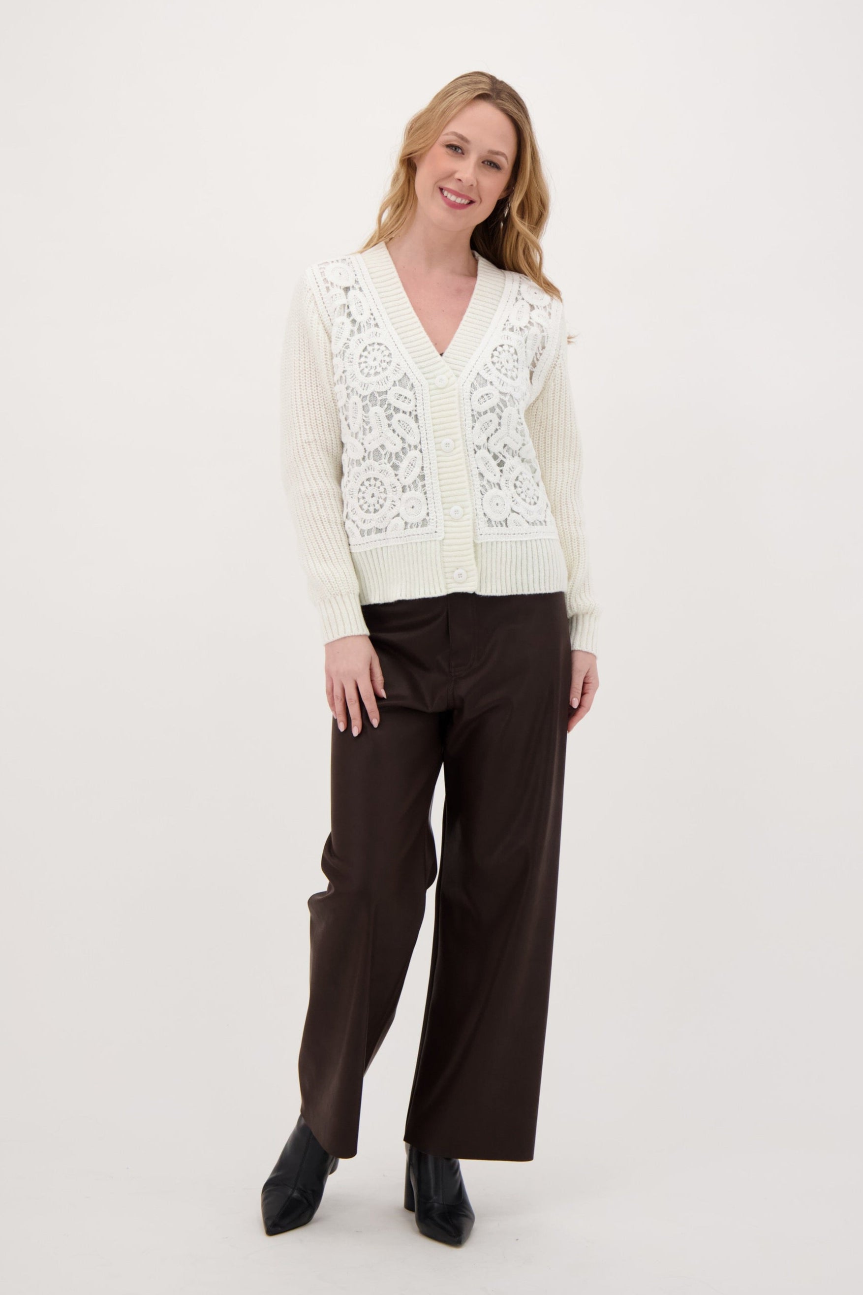 Woman wearing a white embroidered vest and brown pants on a white background