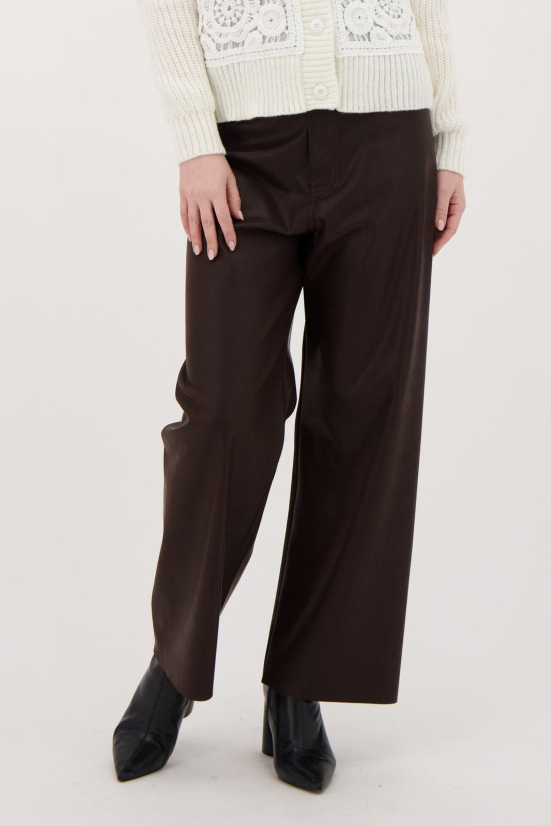 Woman wearing a white embroidered vest and brown pants on a white background