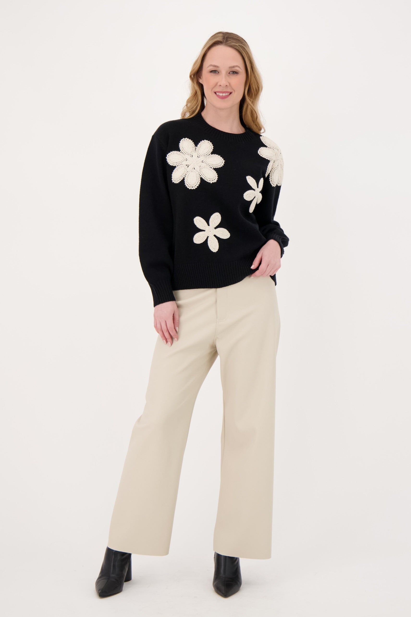Woman wearing a black sweater with white floral patterns and beige pants on a white background
