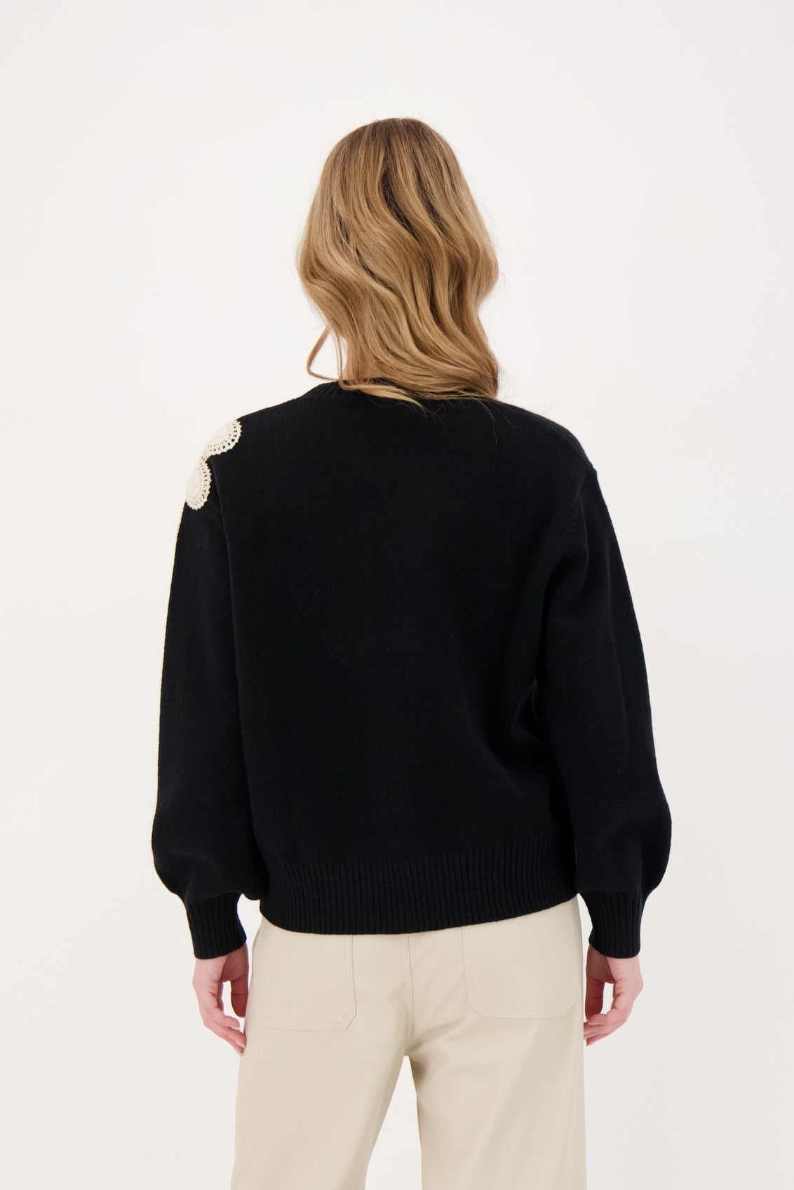Person wearing a black sweater with white patches on a plain background