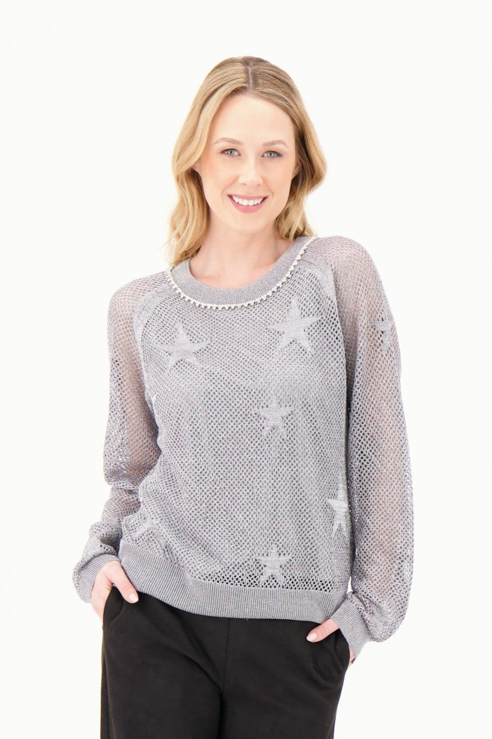 Woman wearing a gray sweater with star patterns and black pants on a white background