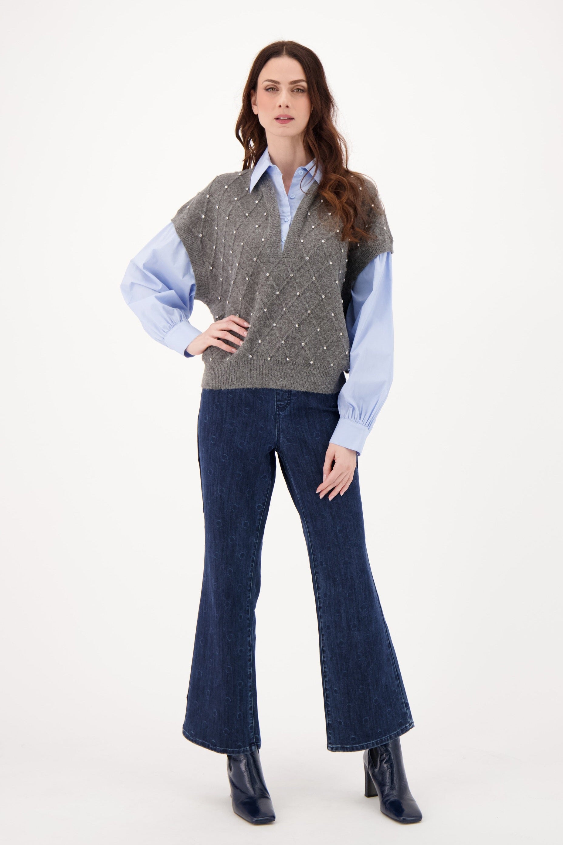 Woman wearing a gray patterned vest over a light blue shirt with dark blue flared jeans on a white background