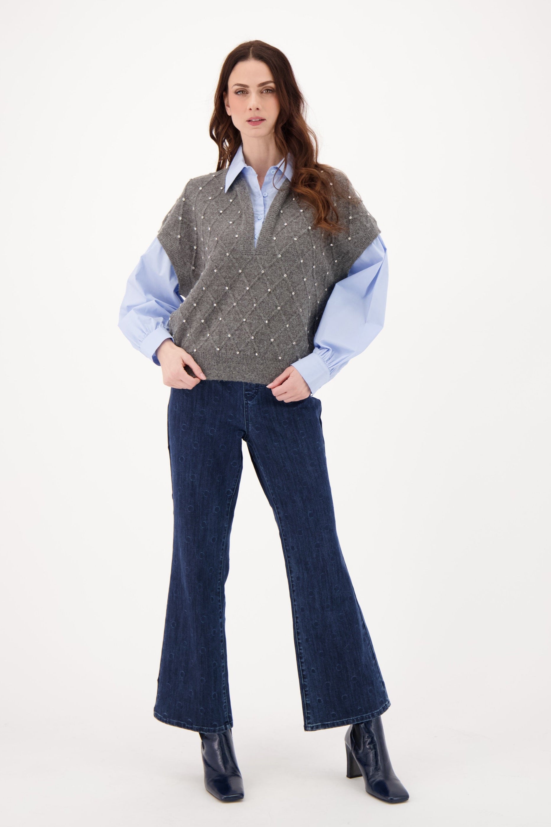 Woman wearing a gray sweater over a blue shirt with flared jeans on a white background