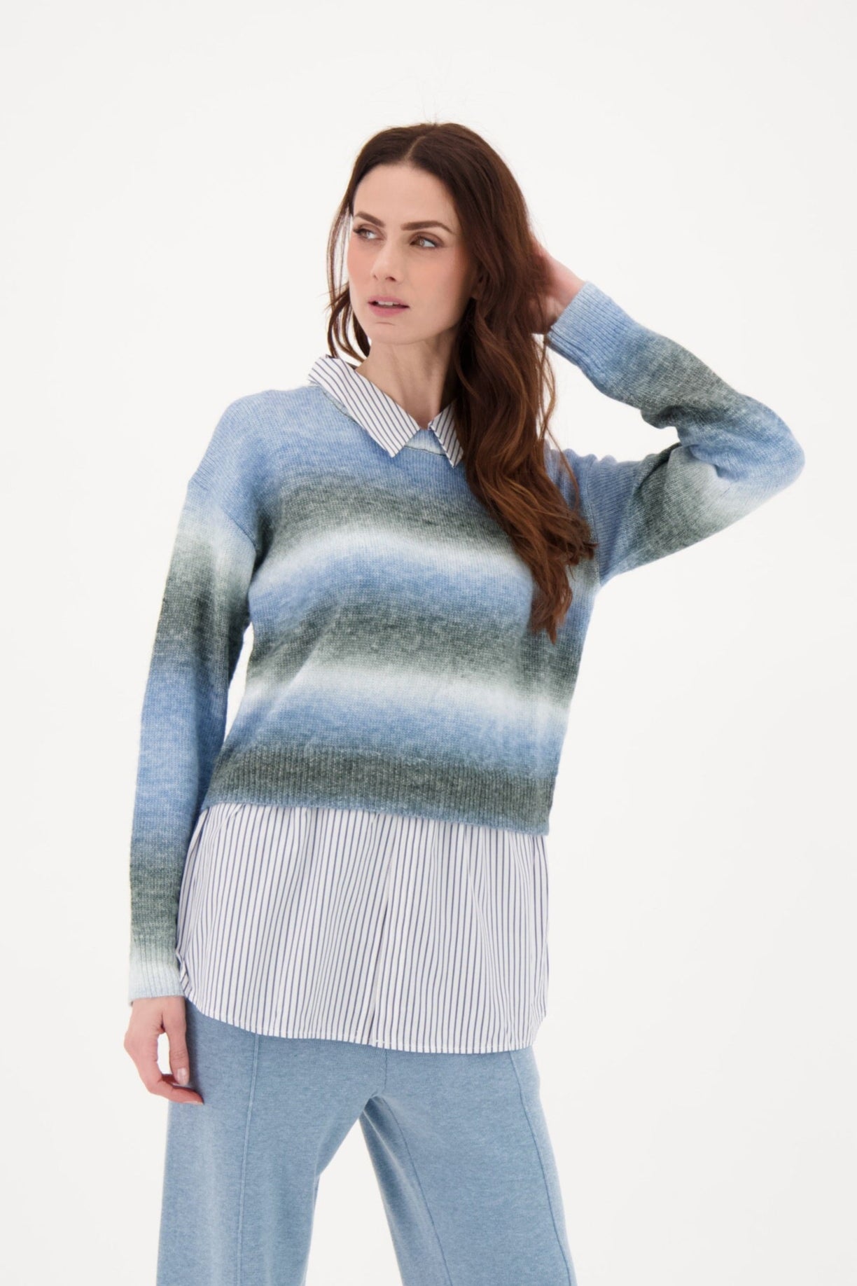 Woman wearing a blue and gray striped sweater with a white shirt underneath on a white background